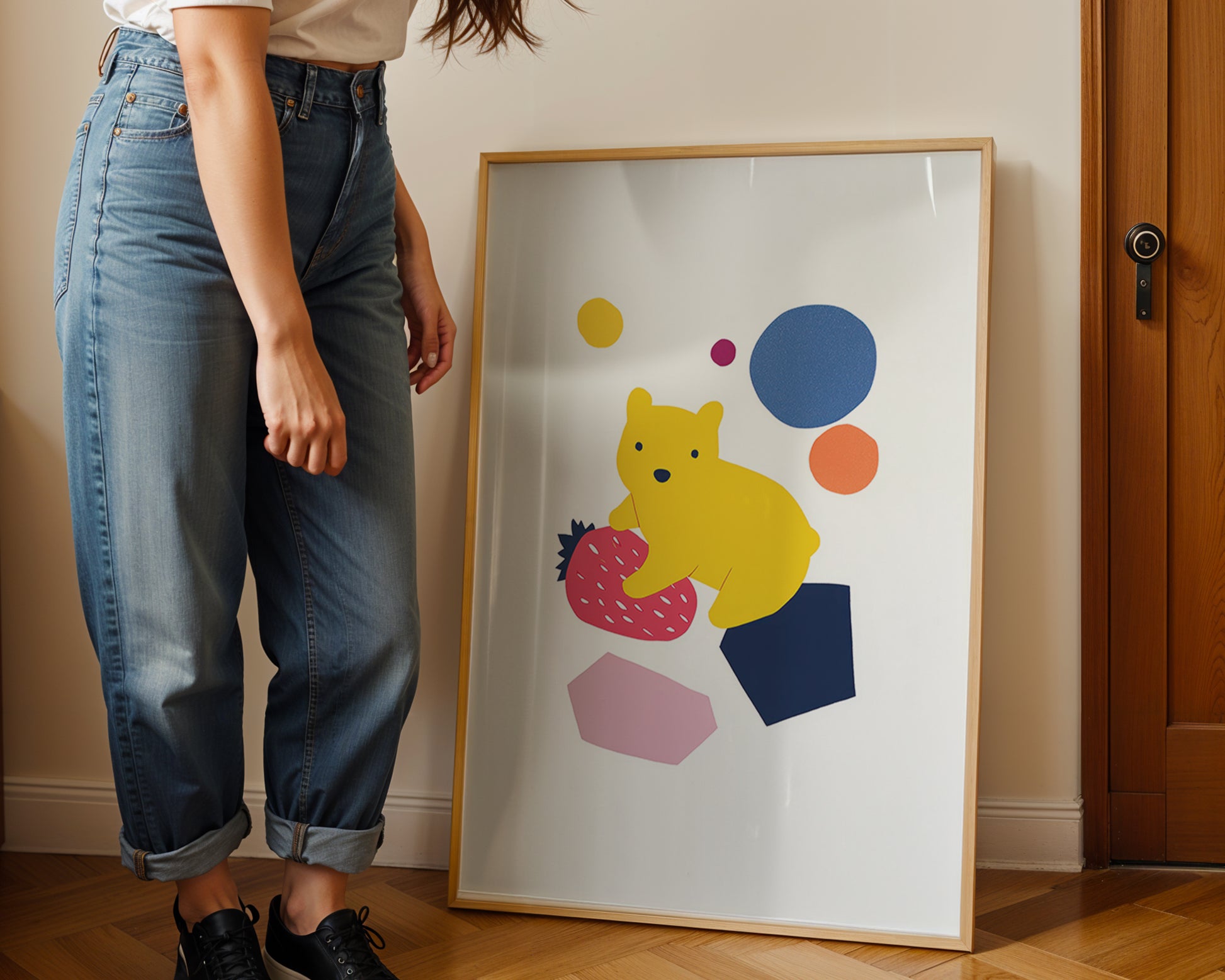 Person standing next to a colorful framed artwork of a bear holding a strawberry.