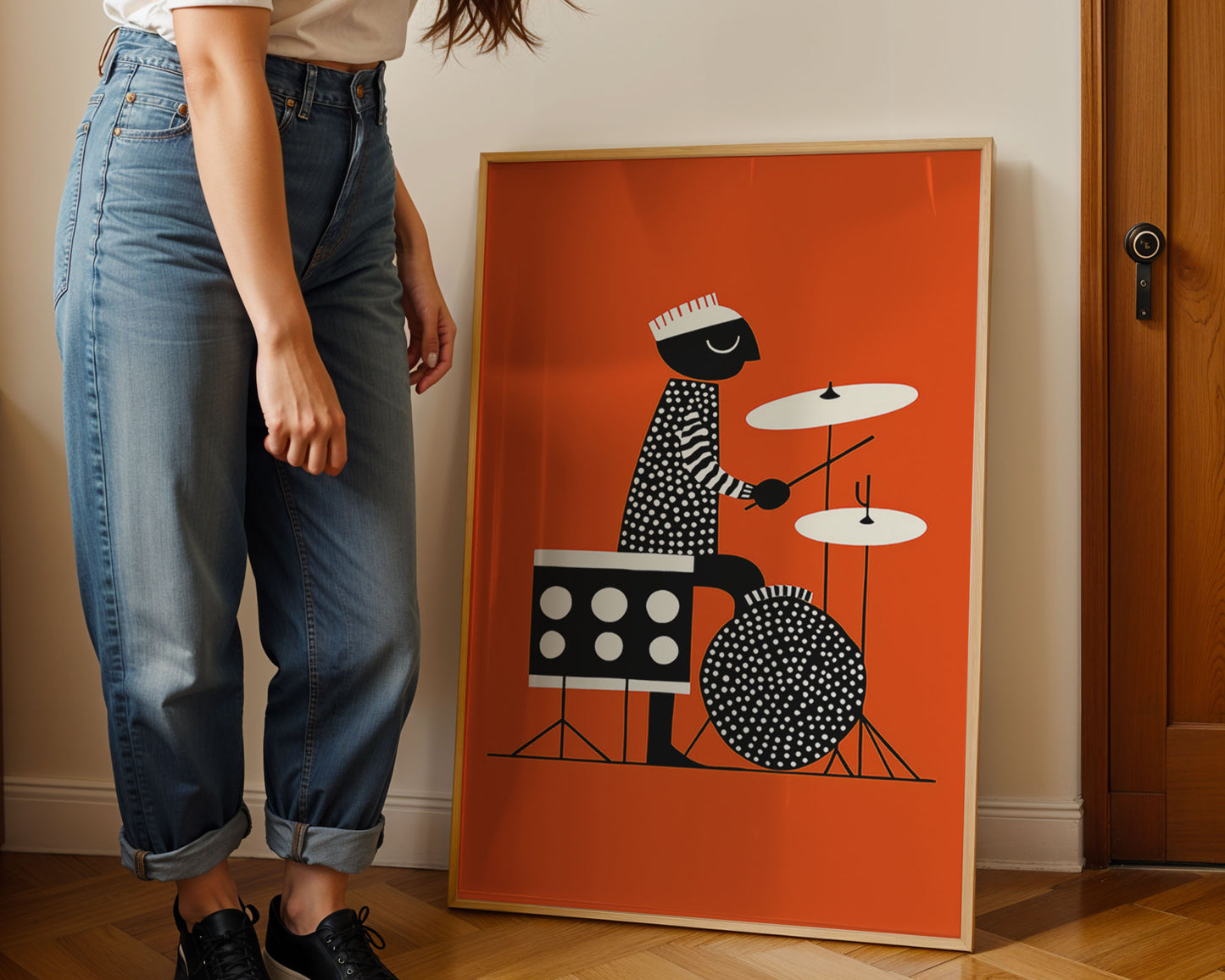 Person wearing jeans standing next to a framed jazz artwork of a person playing drums on an orange background.