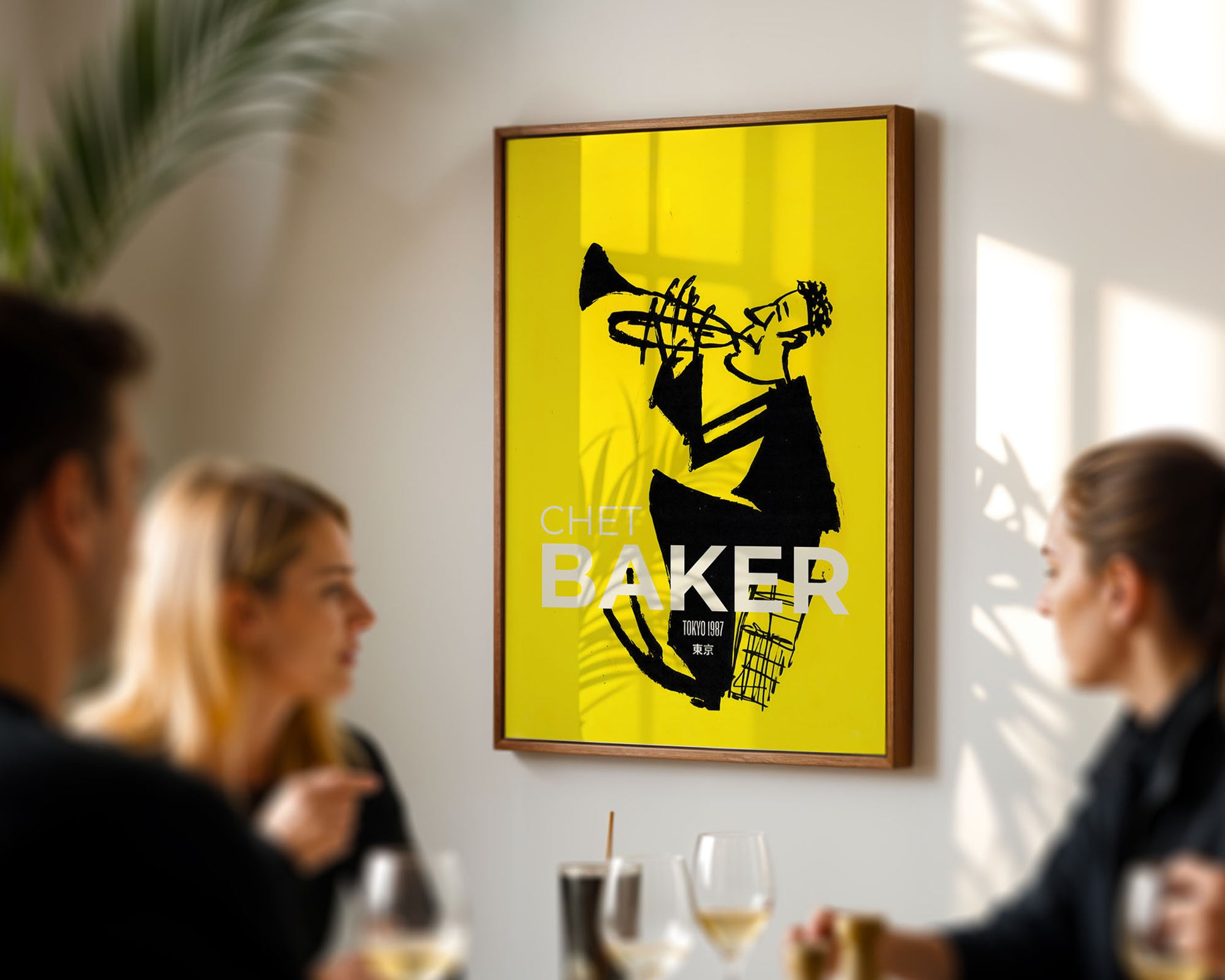 Framed poster of a jazz musician playing a trumpet on a yellow background, hanging in a room with people socializing.