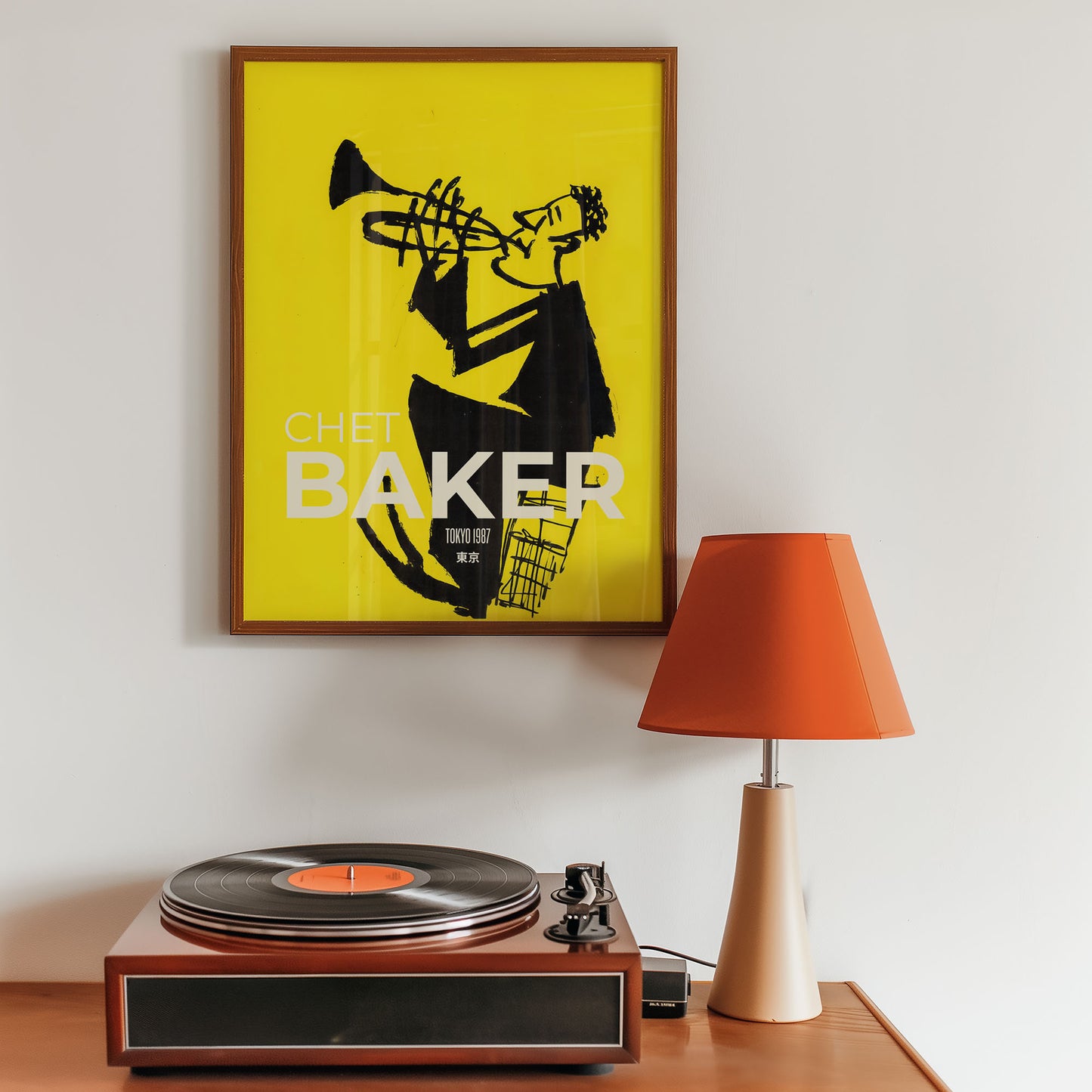 Framed poster inspired by Chet Baker above a turntable with an orange lamp on a wooden surface.