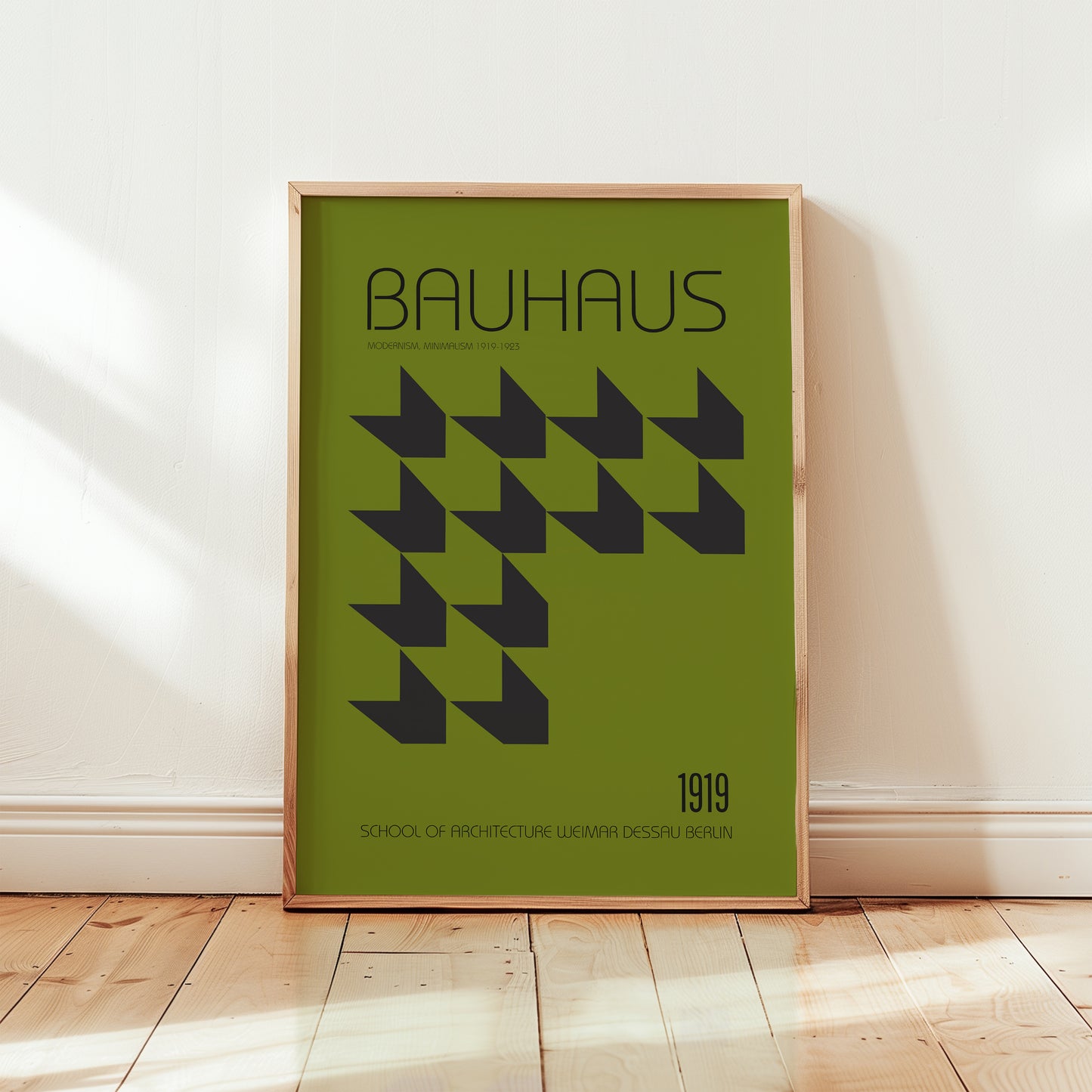 Framed Bauhaus poster with geometric design and text on a green background, leaning against a white wall.