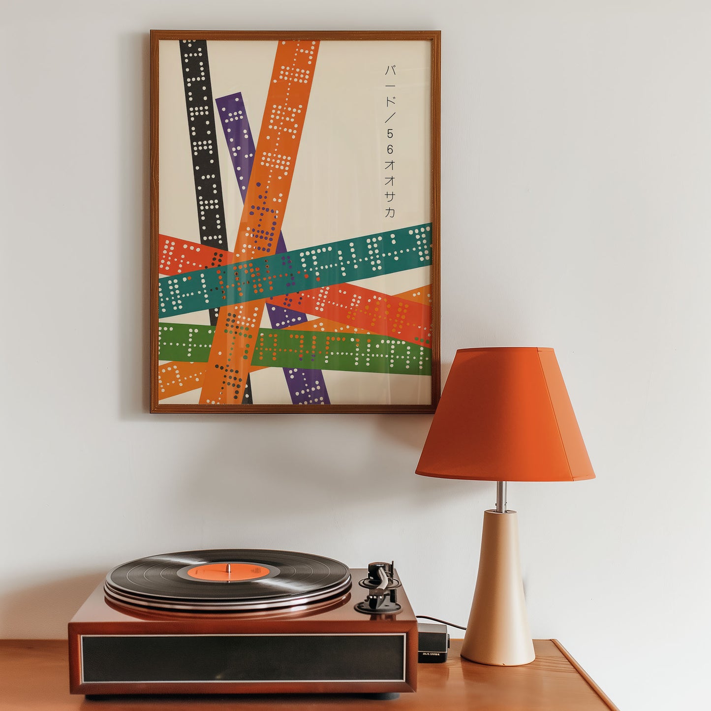 Turntable on a wooden table with a colorful abstract poster and an orange lamp in the background.