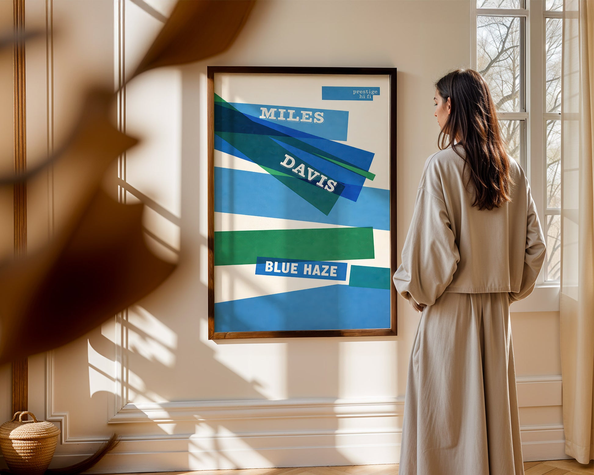 Woman standing in a room looking at a framed Miles Davis 'Blue Haze' album cover on the wall.