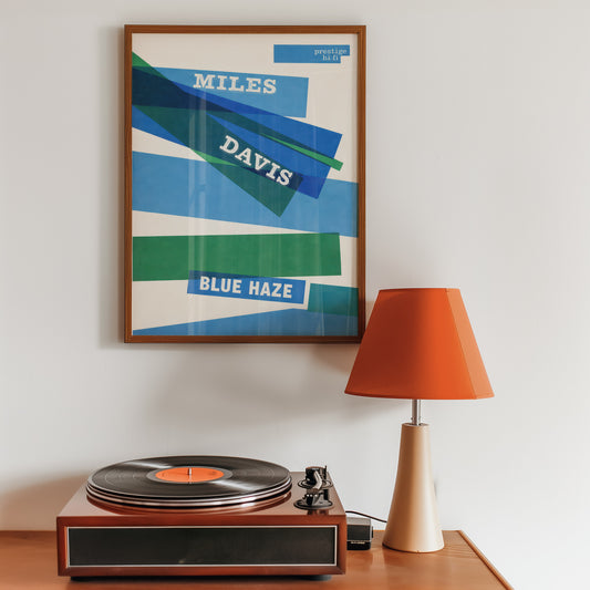 Framed Miles Davis 'Blue Haze' poster above a record player with an orange lamp.