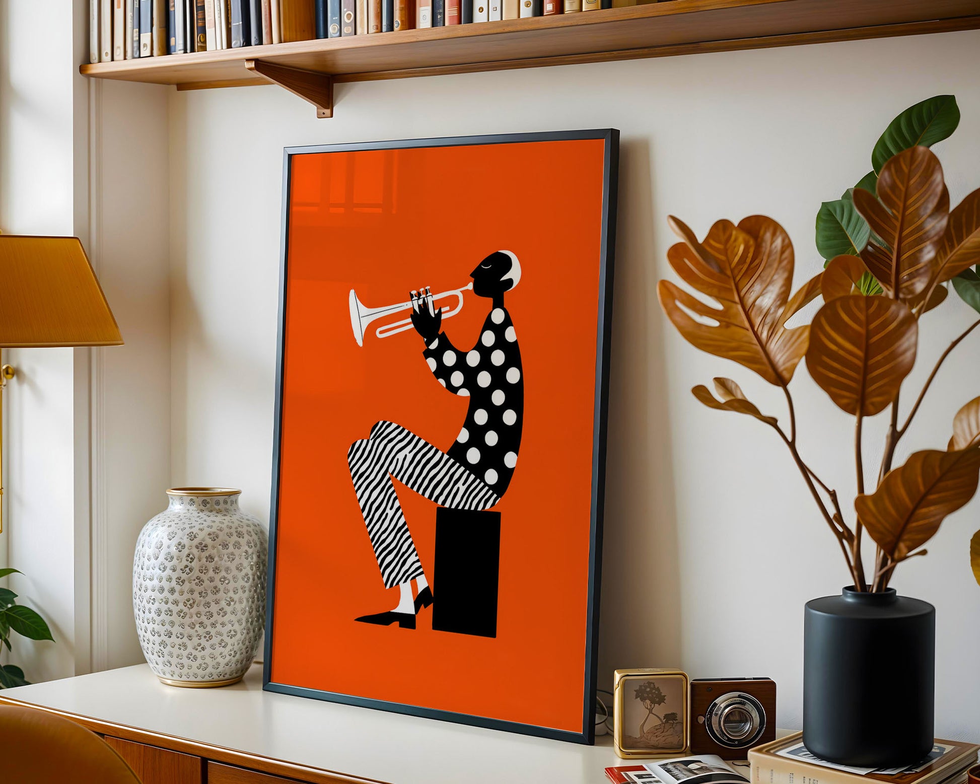 Framed artwork of a person playing a trumpet on an orange background, displayed on a shelf with decorative items.