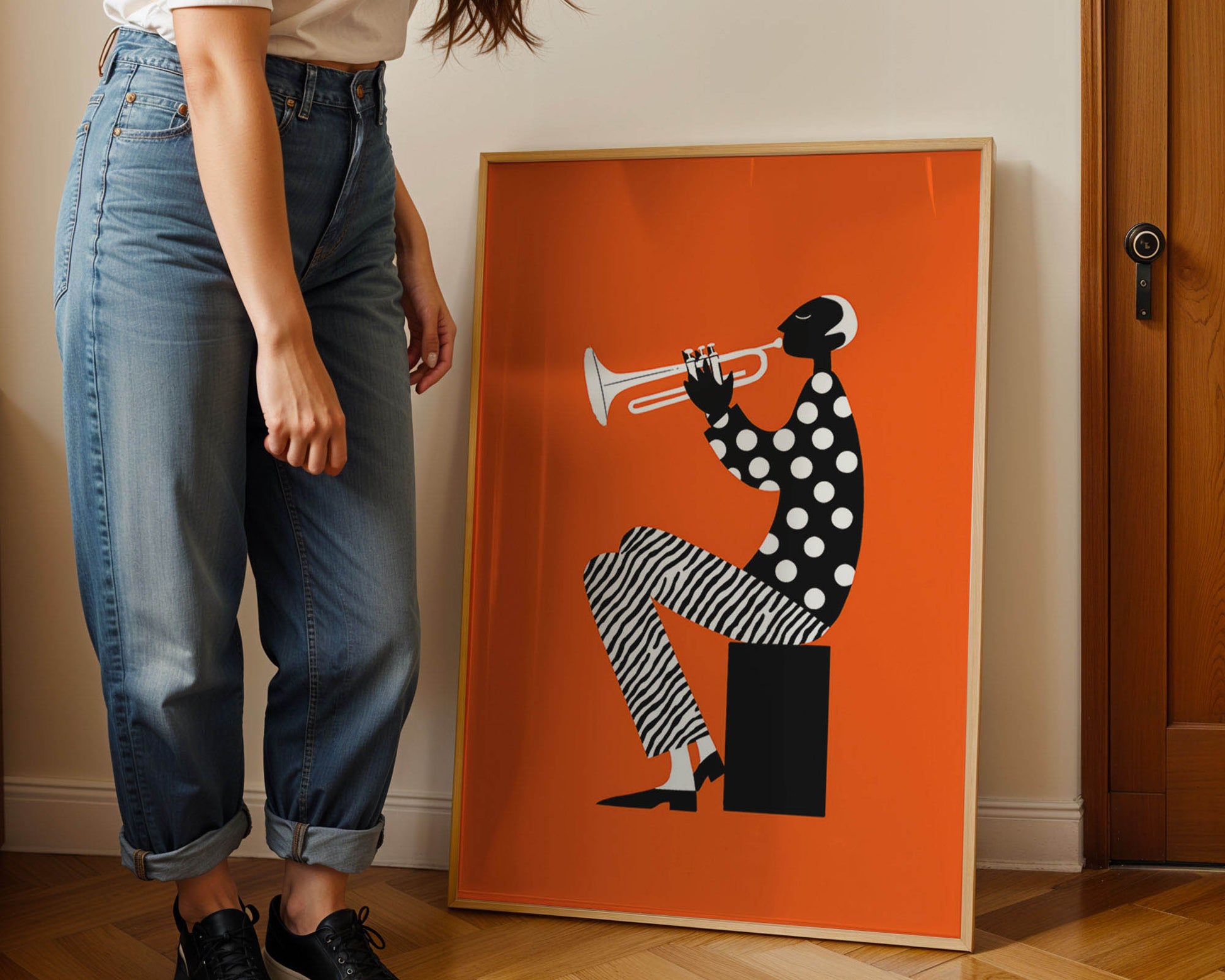 Person standing next to a framed Jazz artwork of a polka-dotted figure playing a trumpet on an orange background.