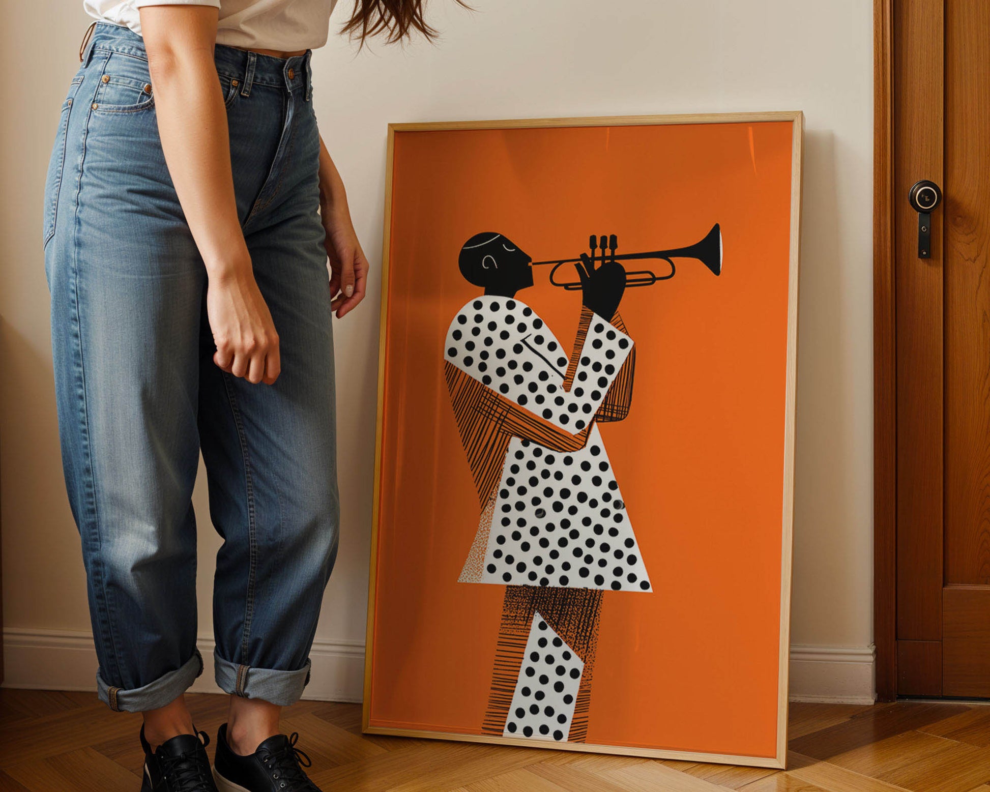 Person standing next to a framed artwork of a person playing a trumpet on an orange background in a Mid-century modern poster styled in clean Scandinavian inspired living space