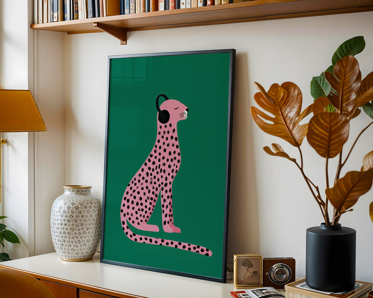 Framed artwork of a pink cheetah on a green background in a home setting with decor elements.
