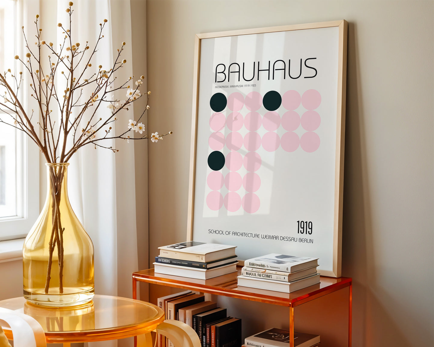 Framed Bauhaus poster on a wall with books and a vase on a table below.