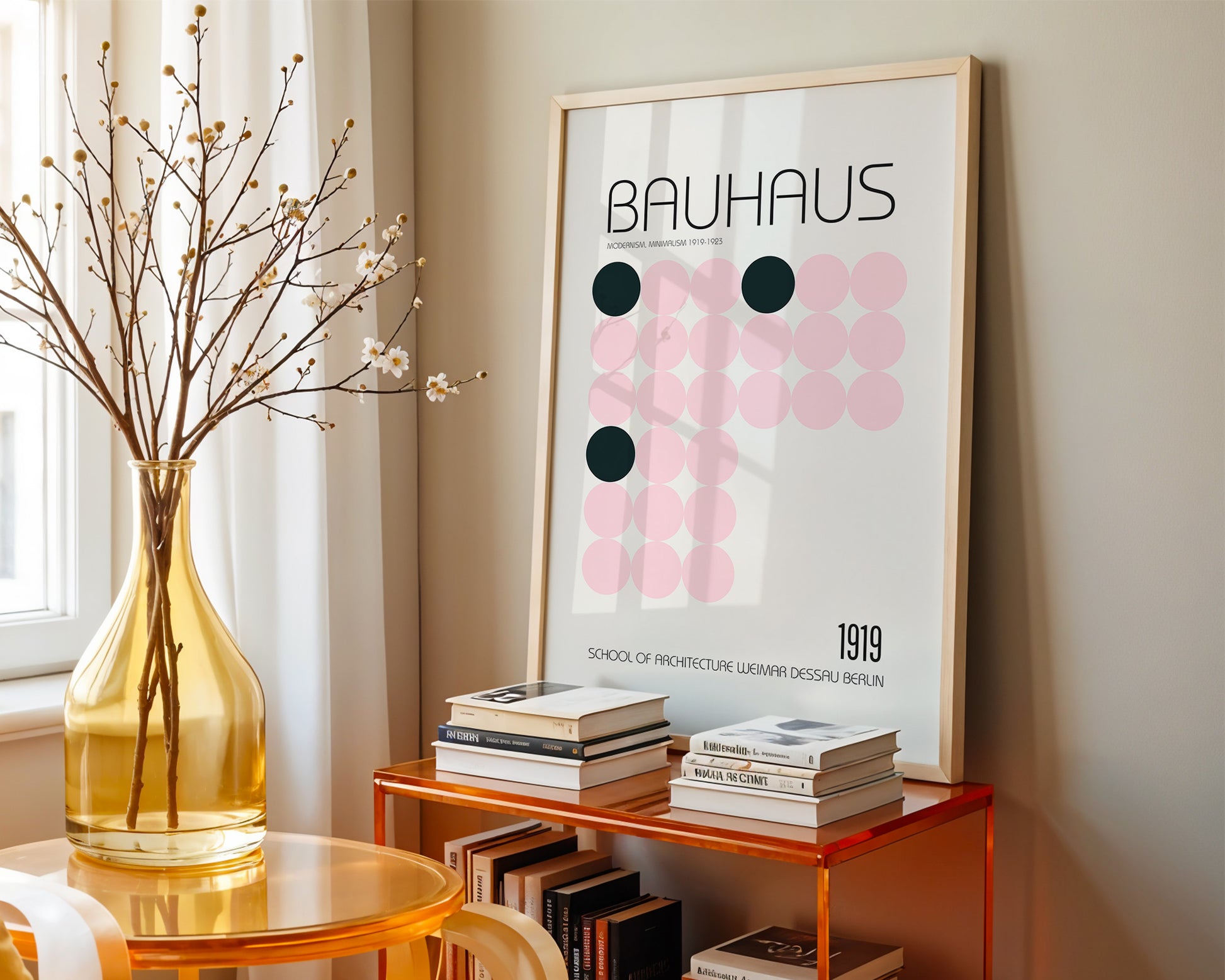 Framed Bauhaus poster on a wall with books and a vase on a table below.