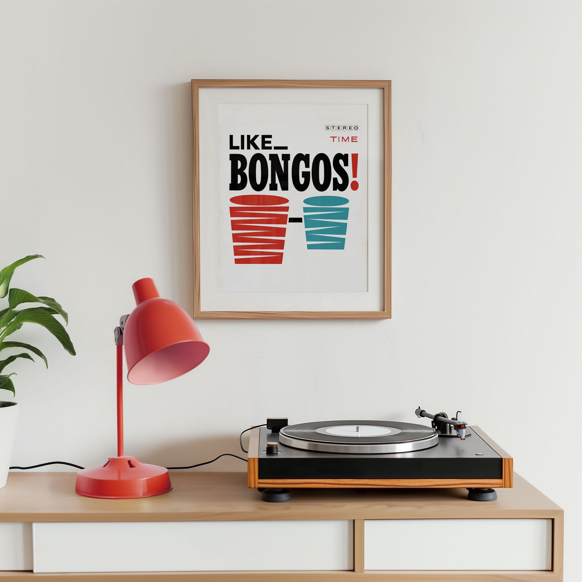 Turntable on a wooden shelf with a red lamp and framed poster on a white wall.