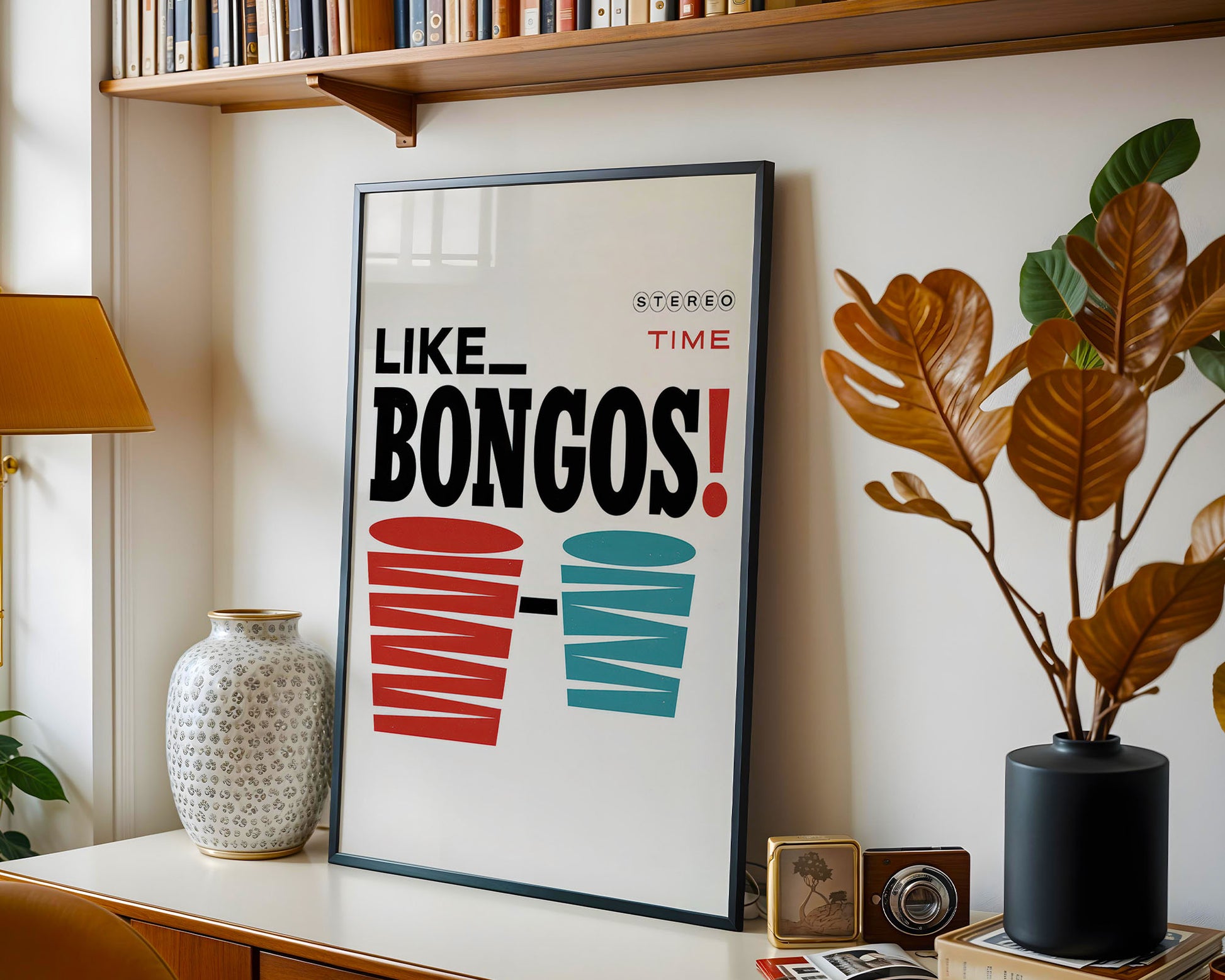 Framed poster with 'LIKE BONGOS!' text on a shelf with books, plants, and decor items.
