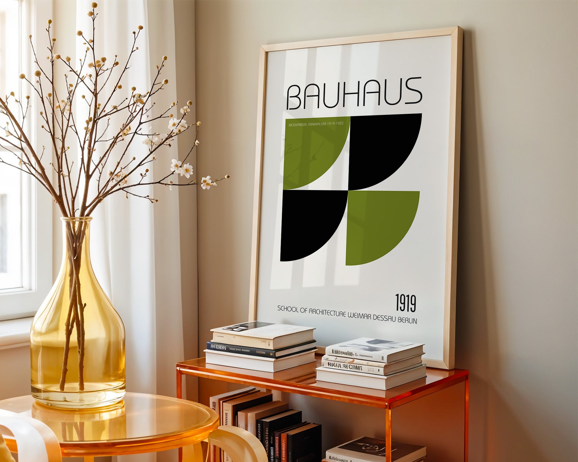 Framed Bauhaus poster on a wall with books and a vase on a table below.