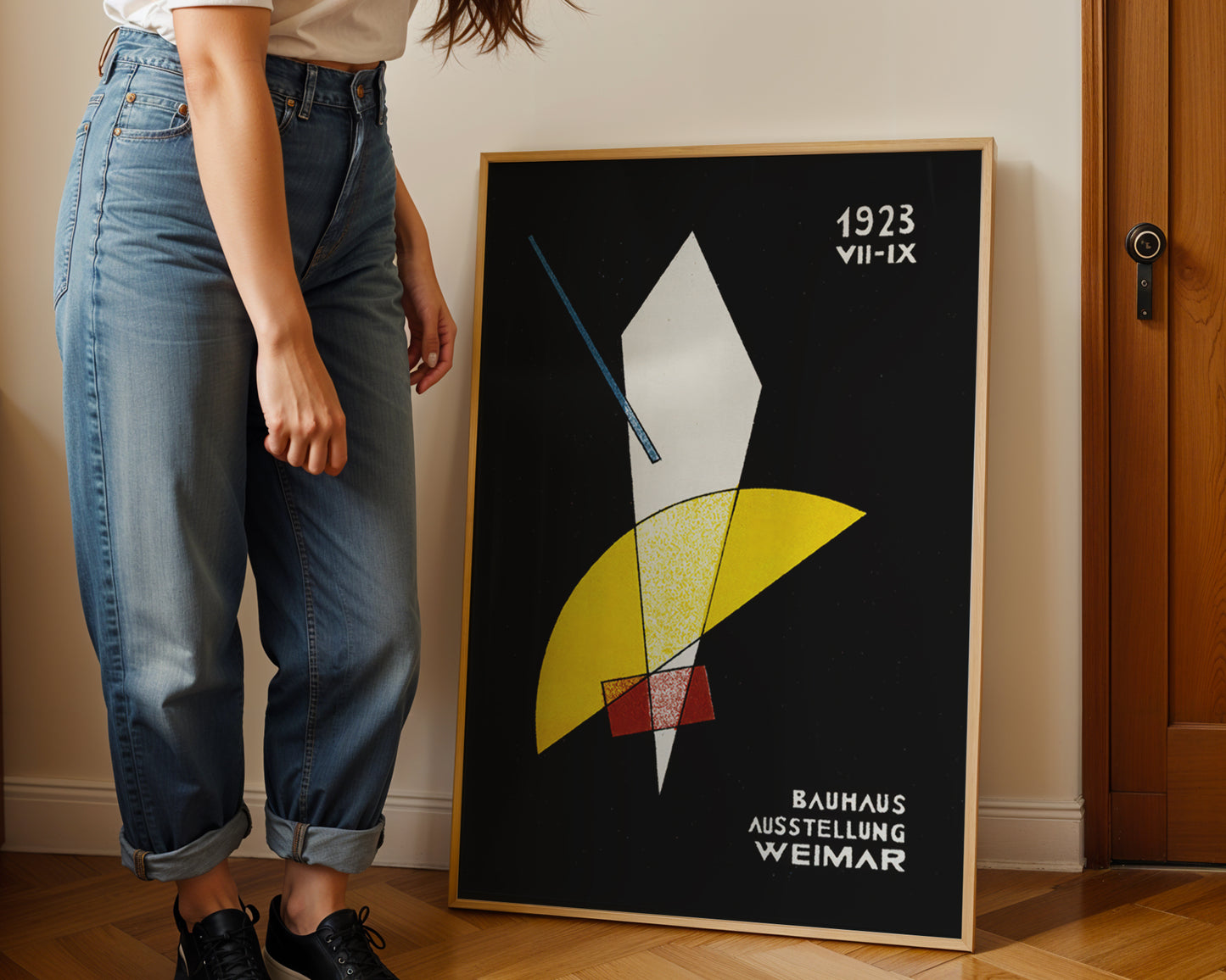 Person standing next to a framed Bauhaus poster on a wall.
