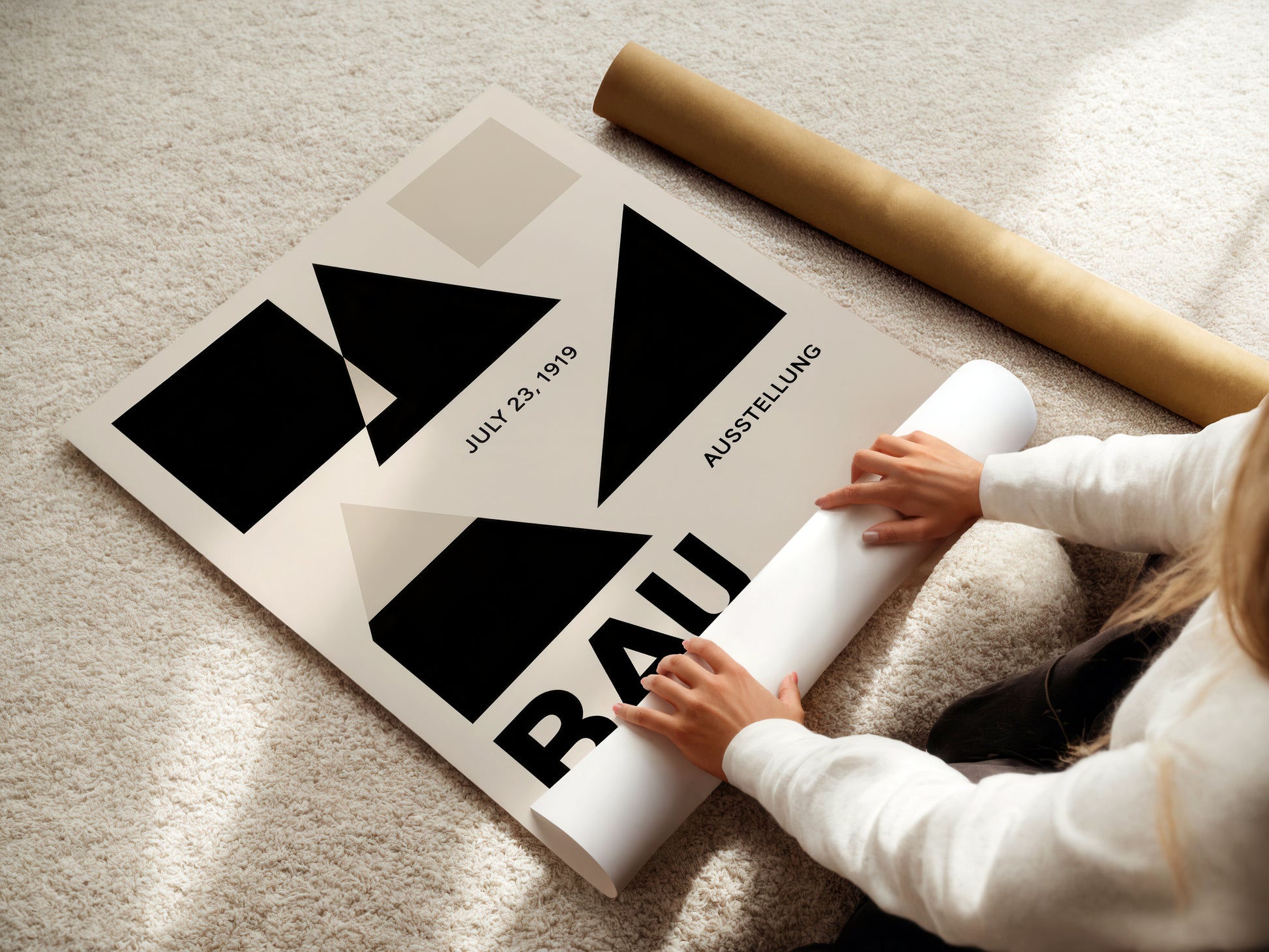 Person unrolling a poster with Bauhaus design on a light-colored floor.