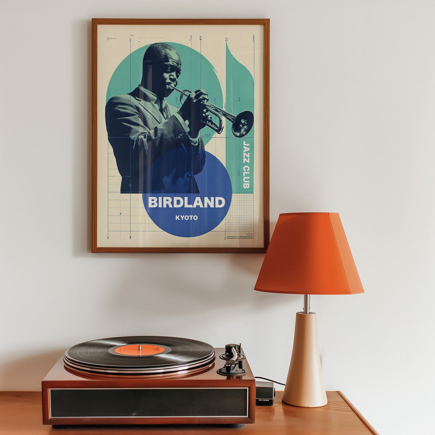 Framed poster of a jazz musician playing a trumpet above a turntable with a lamp on a wooden surface.