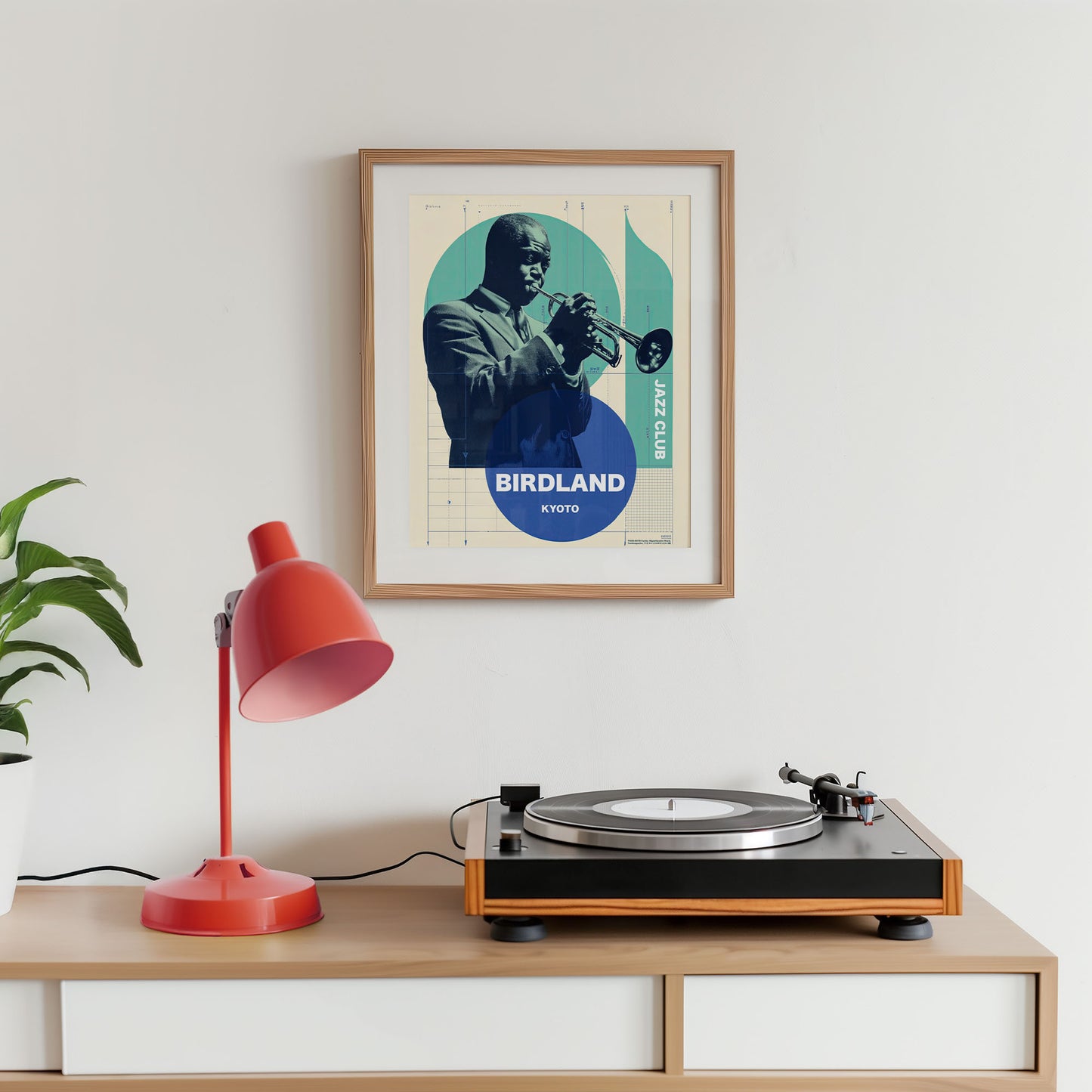 Turntable on a wooden shelf with a framed poster of a musician playing a trumpet on a white wall.