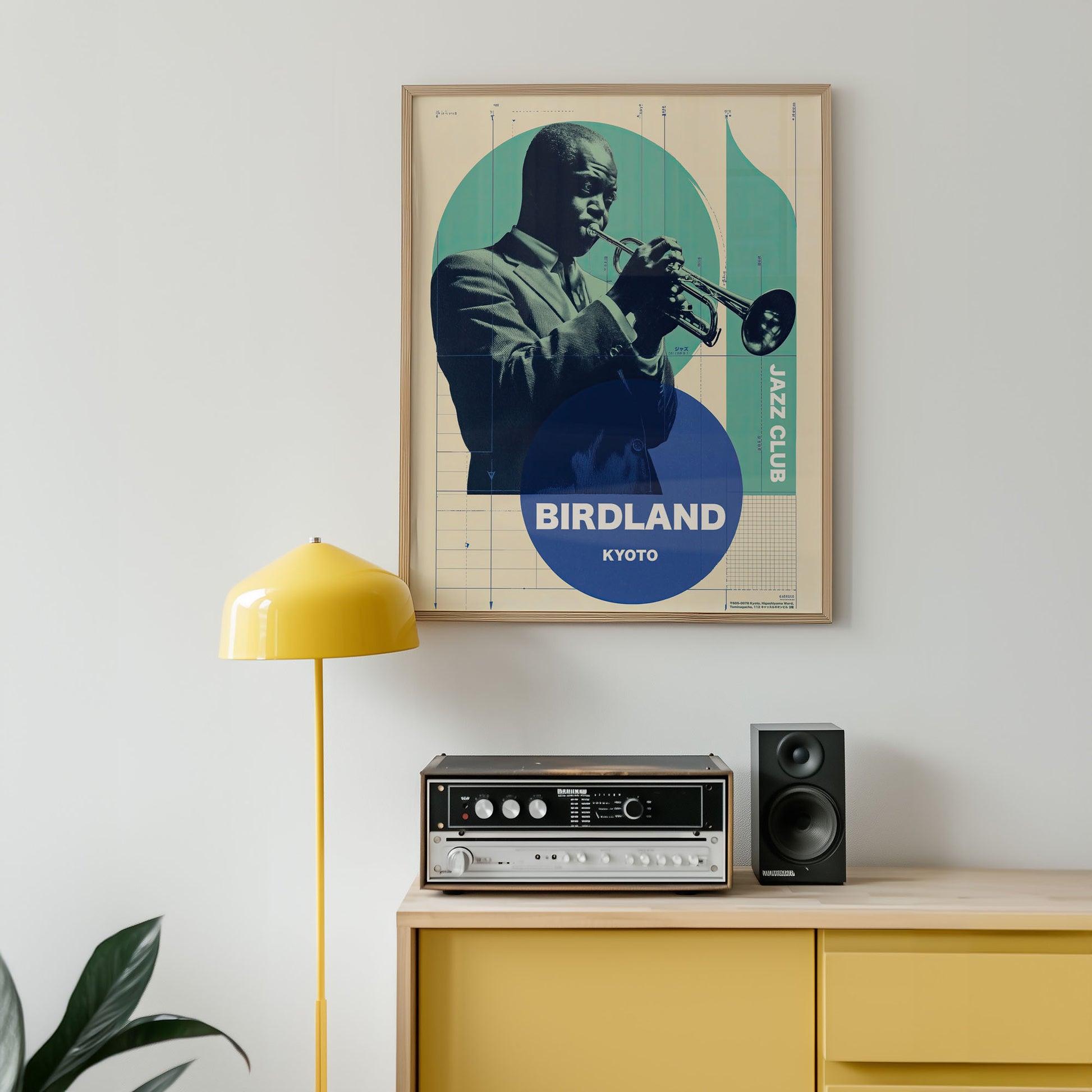 Framed poster of a jazz musician playing a trumpet on a wall above a yellow cabinet with speakers and a lamp.