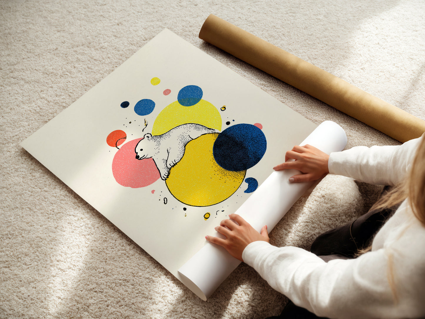 Person unrolling a colorful poster of a bear with abstract shapes on a light-colored floor.