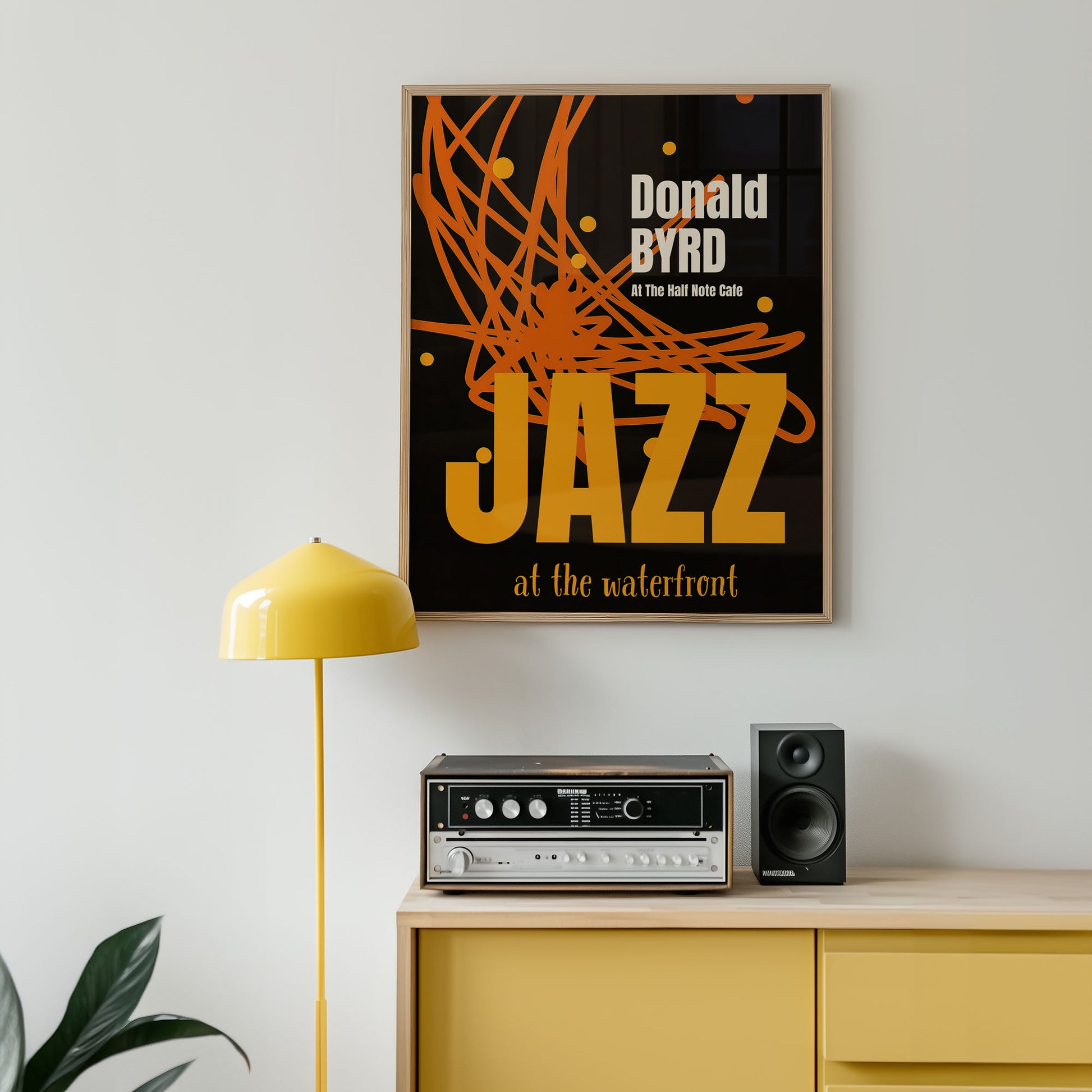 Framed poster with 'Donald Byrd Jazz at the waterfront' text in a room with a yellow lamp and wooden cabinet.