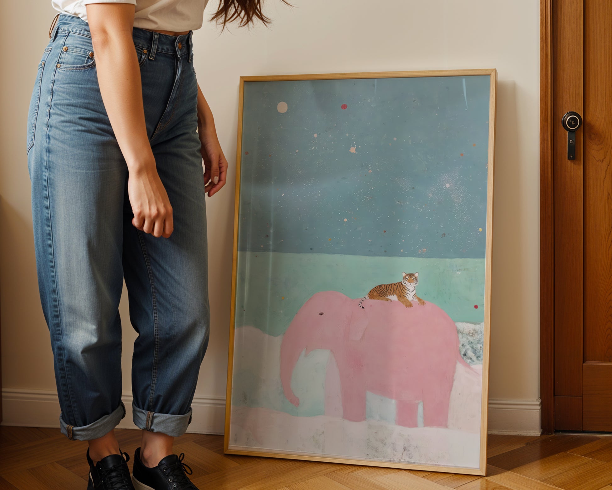Person standing next to a framed illustration of a pink elephant and a cat on a cloud.