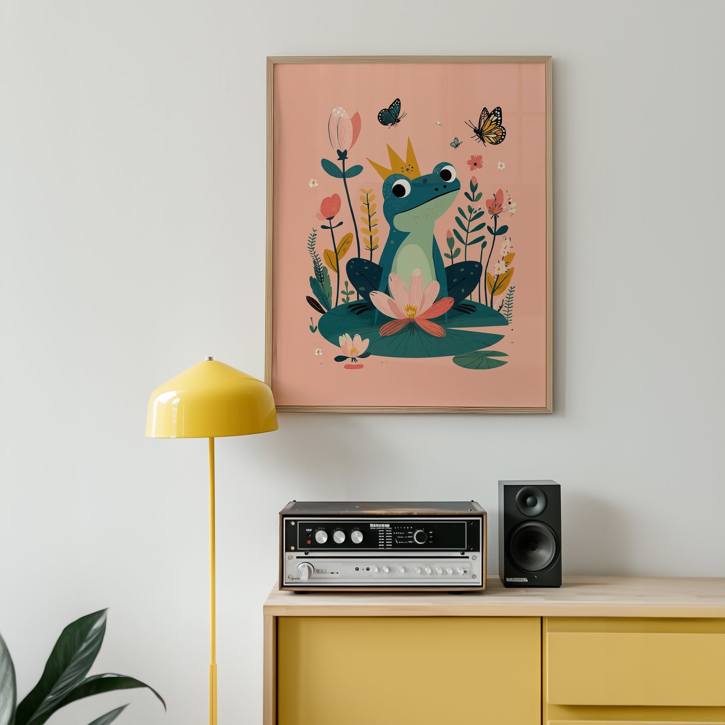 Framed artwork of a frog and flowers on a wall above a yellow cabinet with electronic equipment.