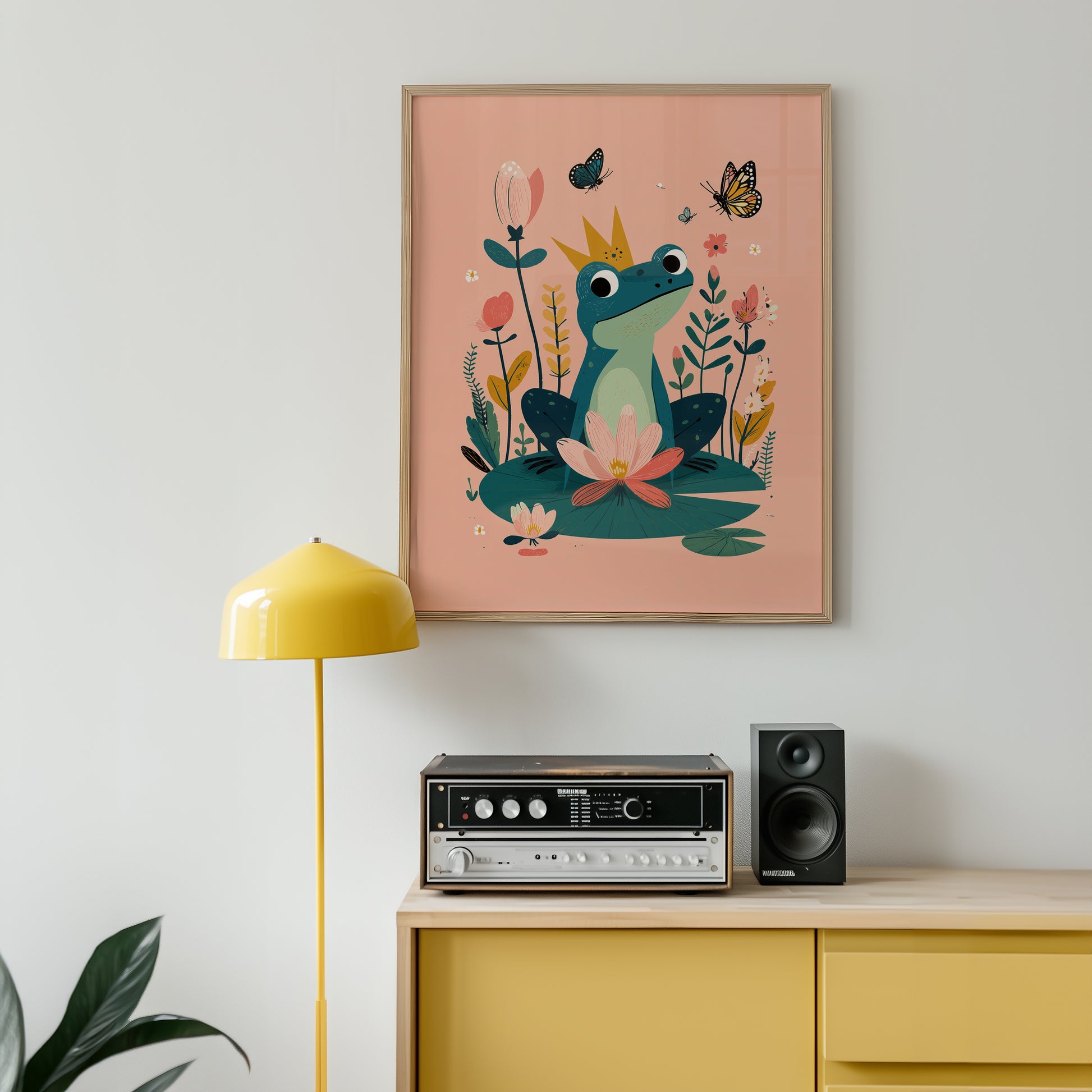 Framed artwork of a frog and flowers on a wall above a yellow cabinet with electronic equipment.
