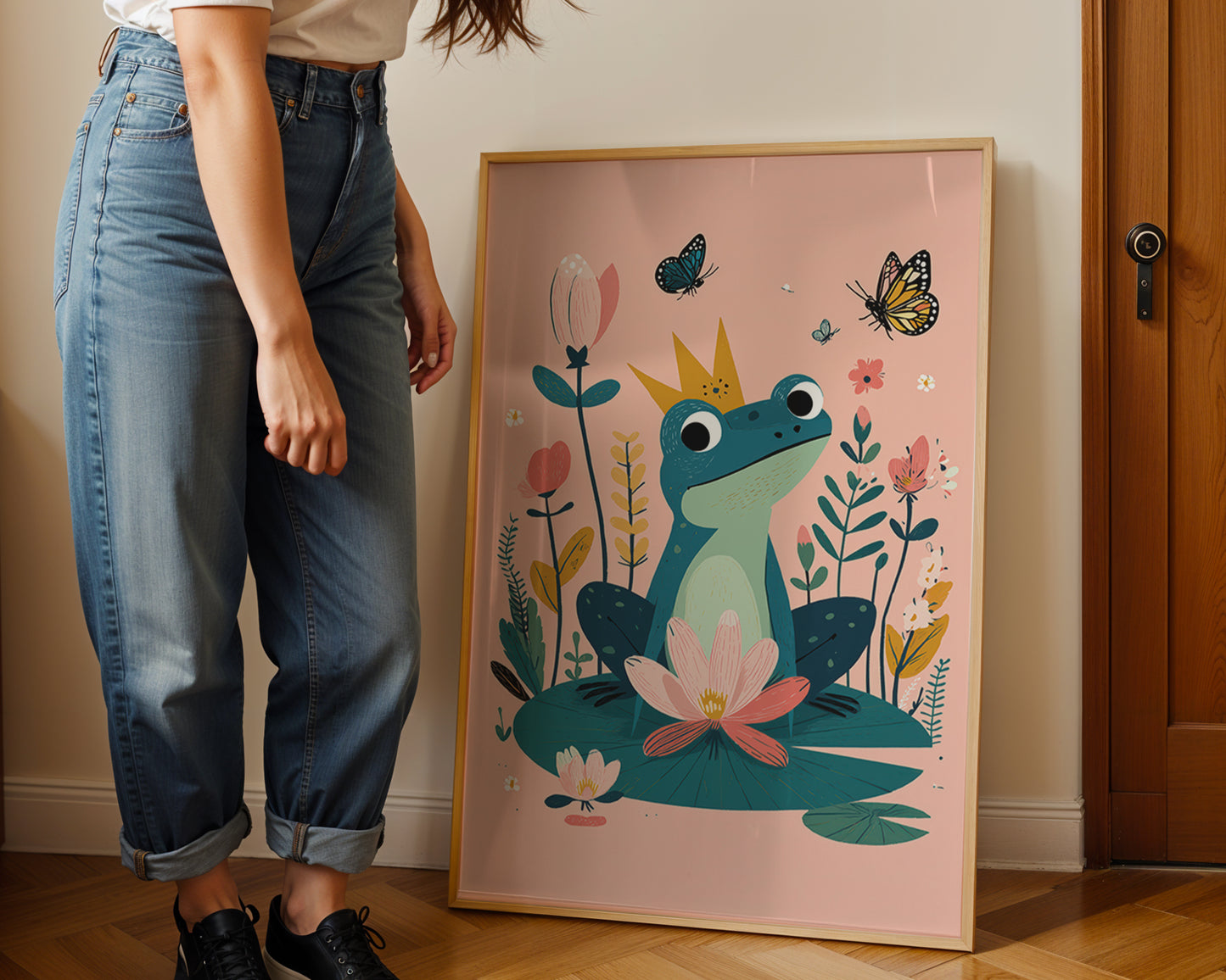 Person standing next to a framed illustration of a frog prince on a pink background