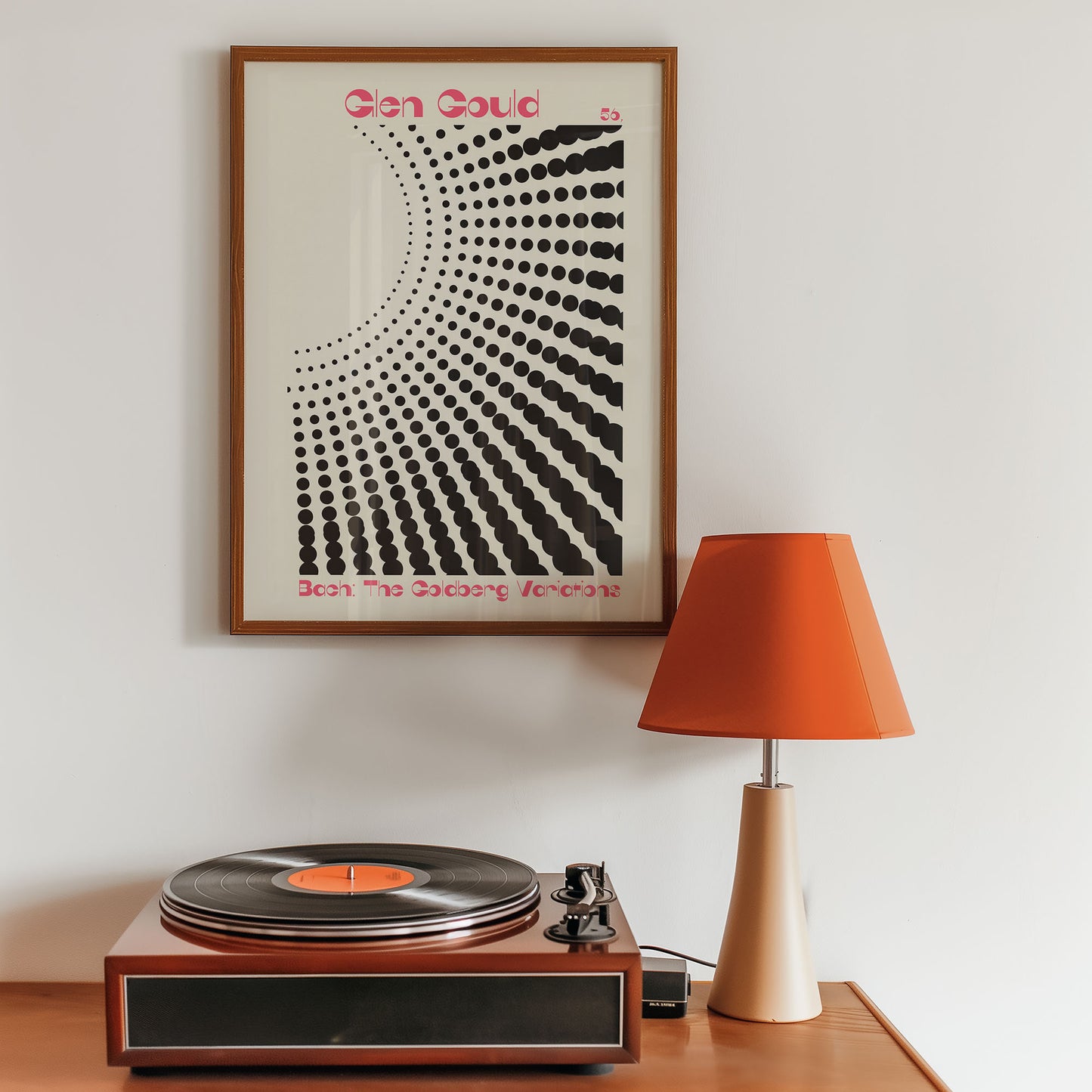 Turntable with a vinyl record, framed poster on the wall, and orange lamp on a wooden surface.