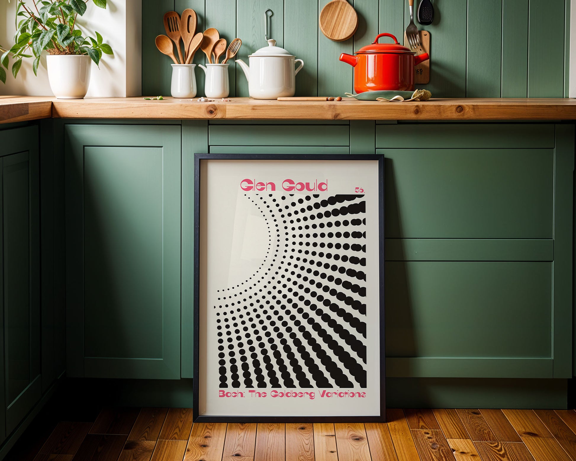 Framed artwork on a kitchen wall with green cabinets and wooden countertop.