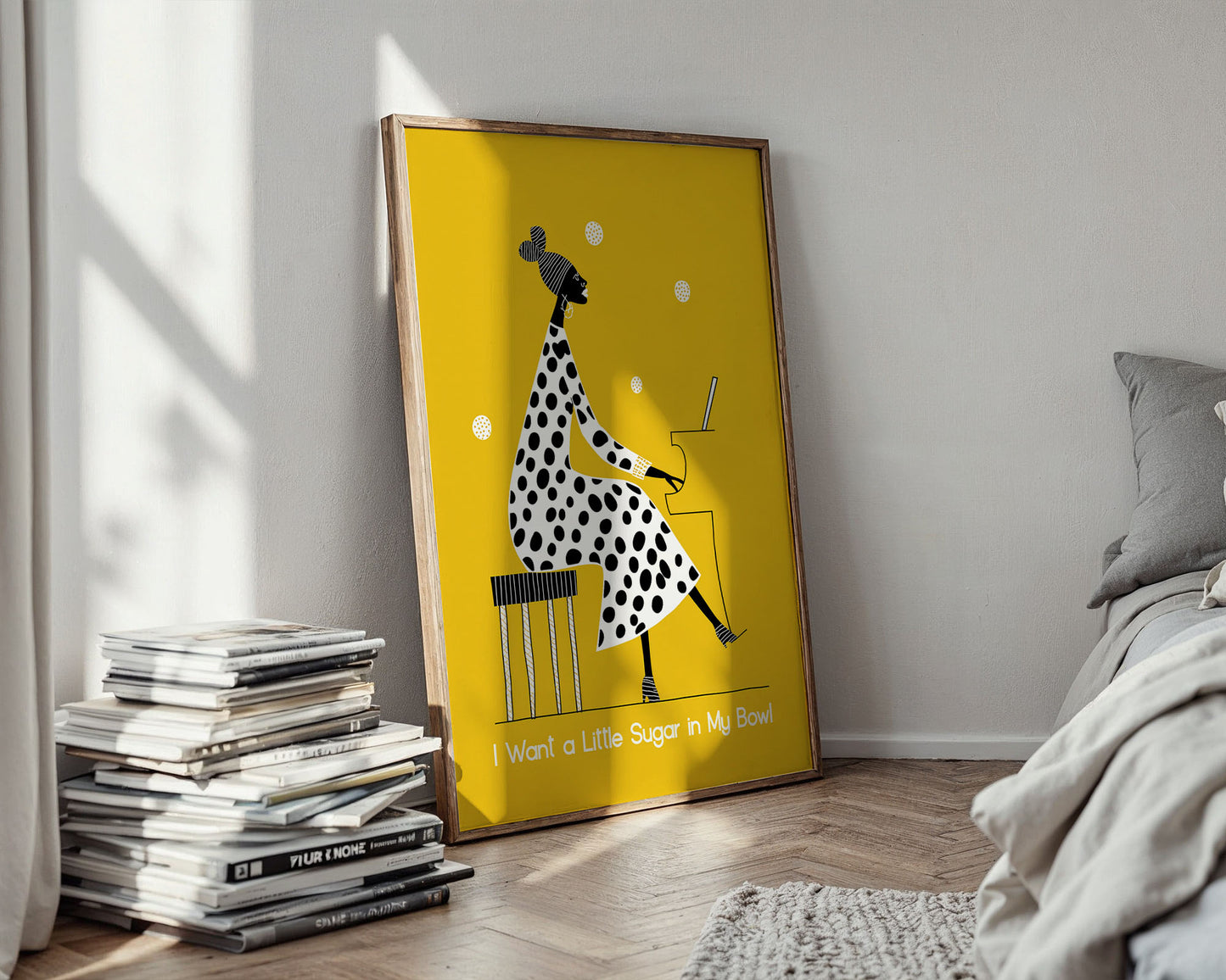 Framed artwork with a polka dot dress design on a yellow background, placed in a room with books and a bed.