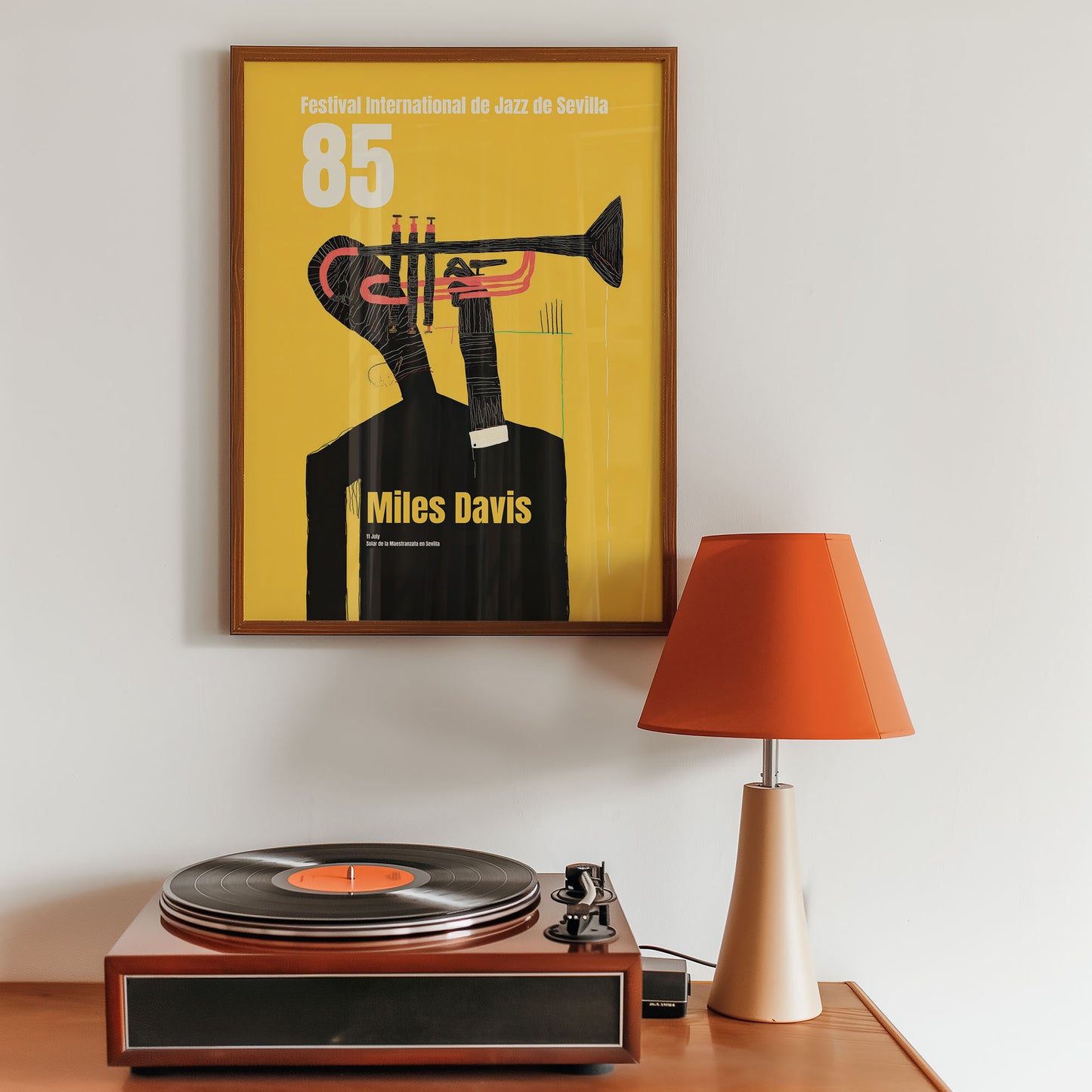 Framed Miles Davis poster above a turntable with an orange lamp on a wooden surface.