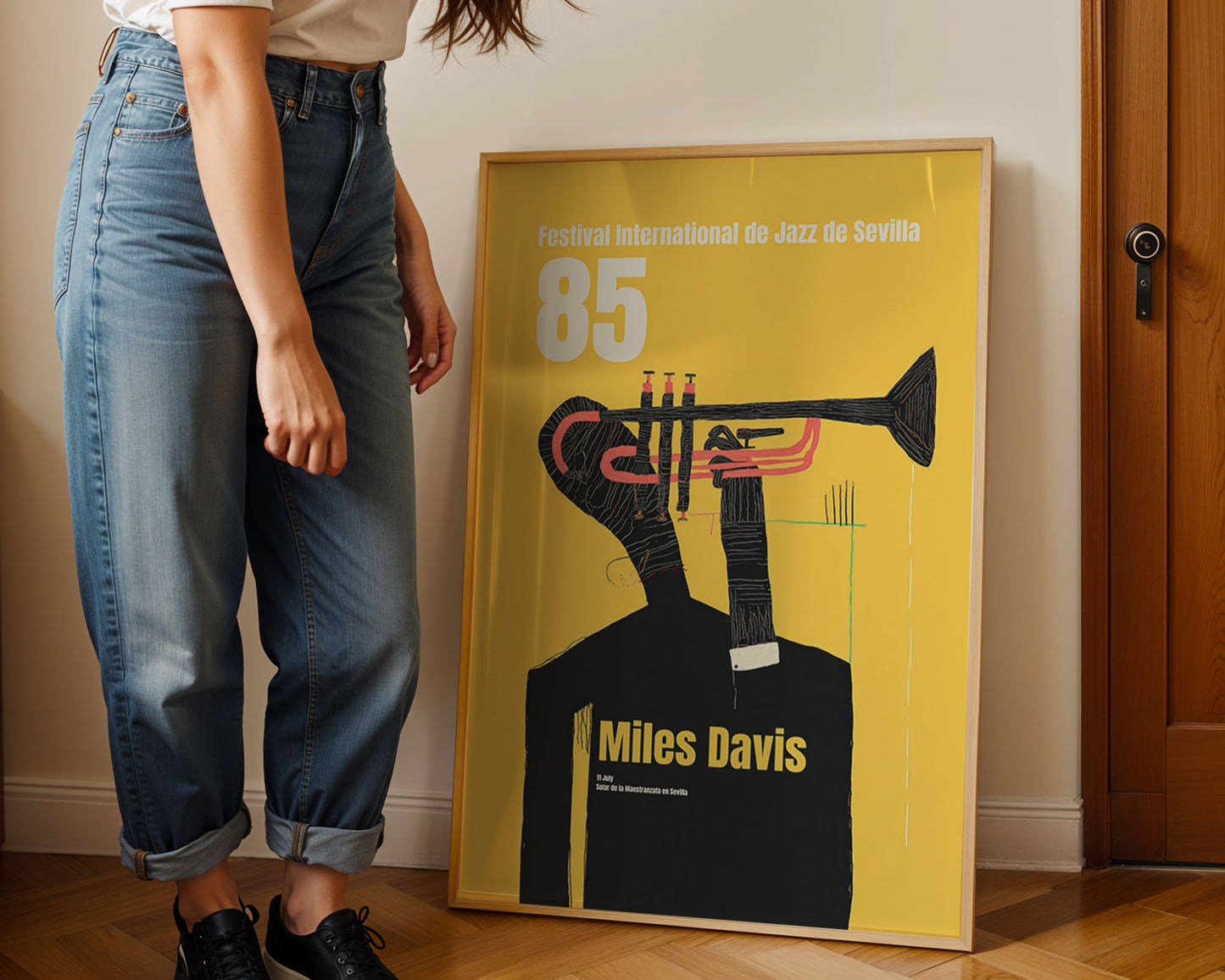 Person standing next to a framed poster of Miles Davis with a yellow background and black trumpet illustration.