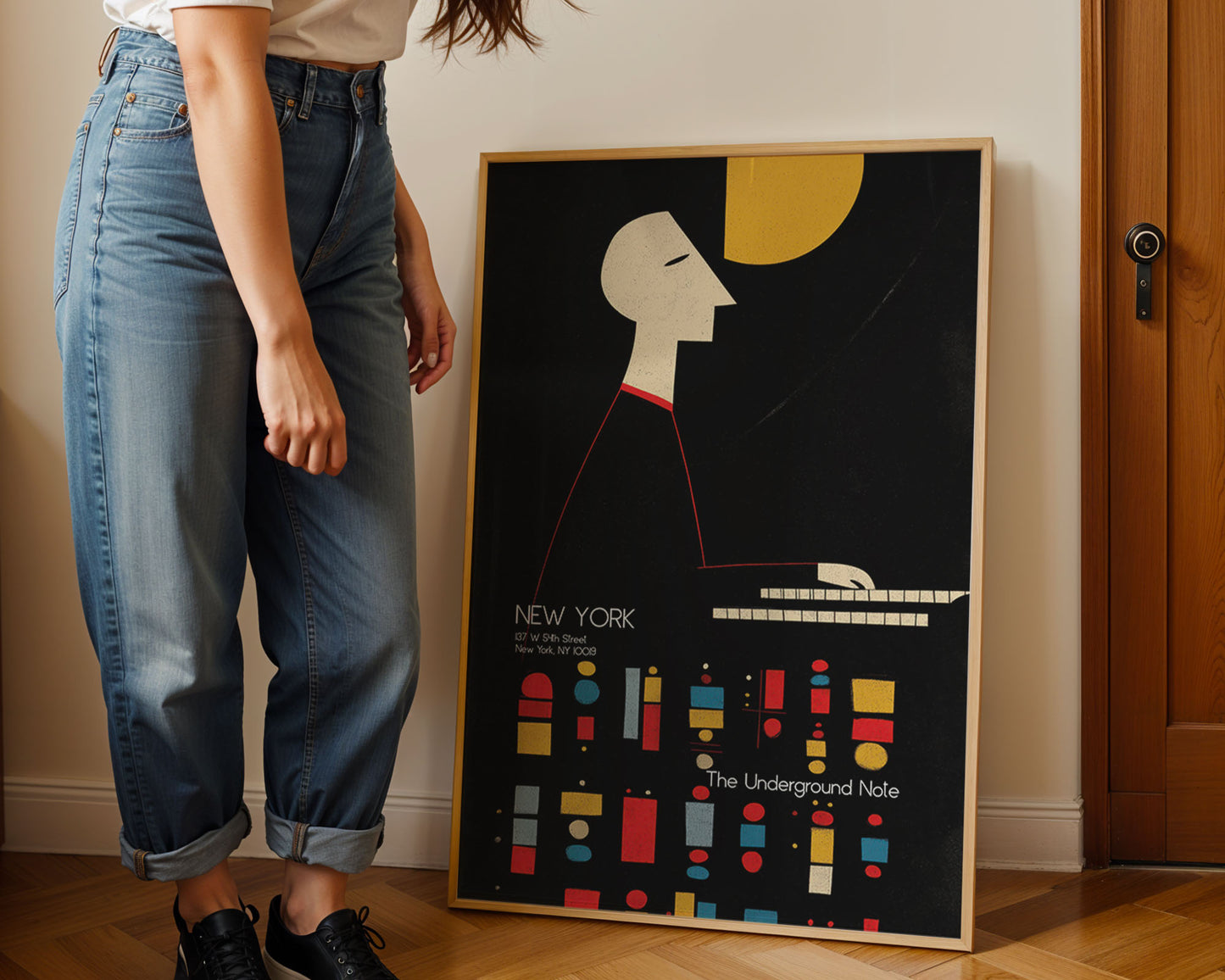 Person standing next to a framed poster with a stylized face and colorful design on a wall.
