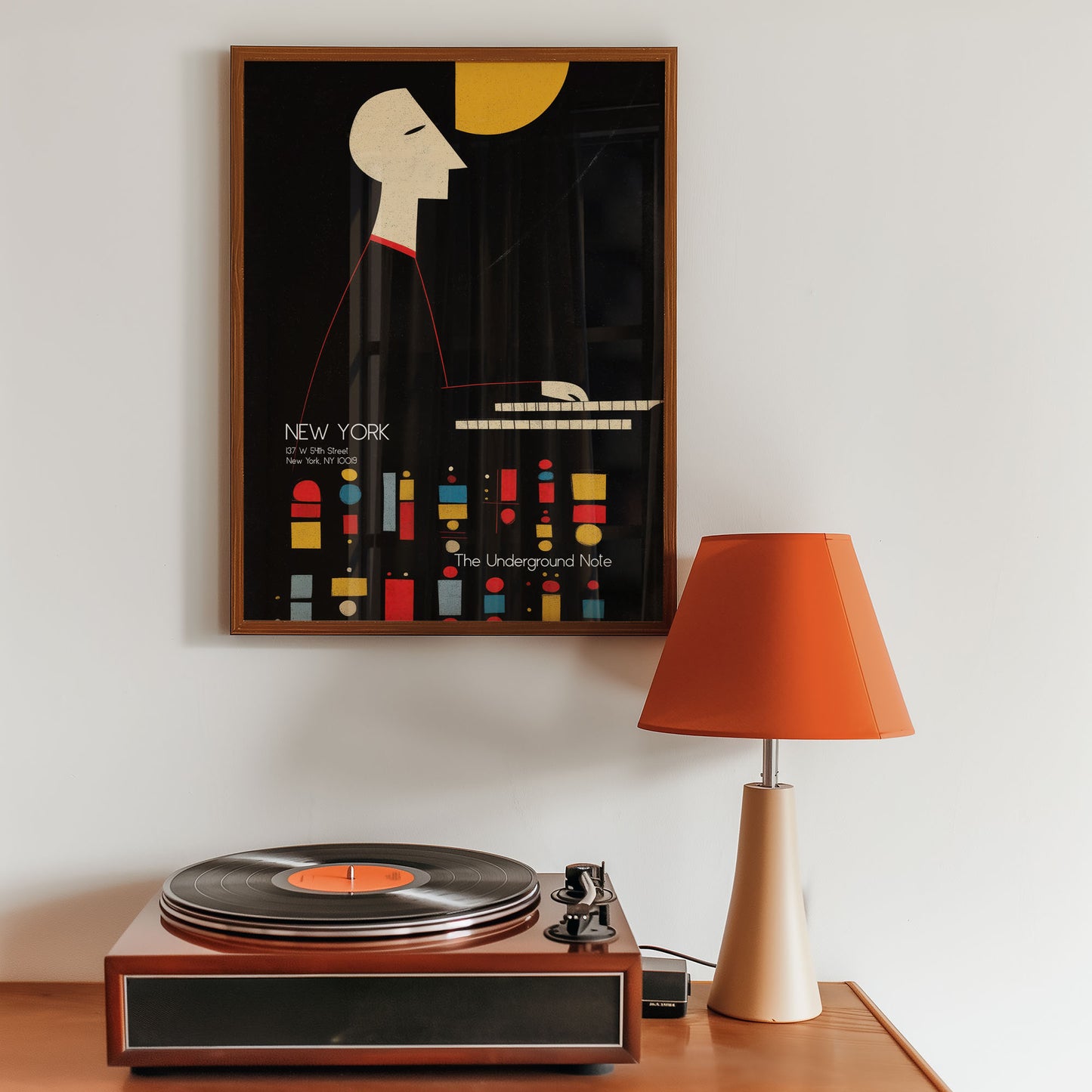 Framed poster of a stylized cityscape on a wall above a turntable with an orange lamp.