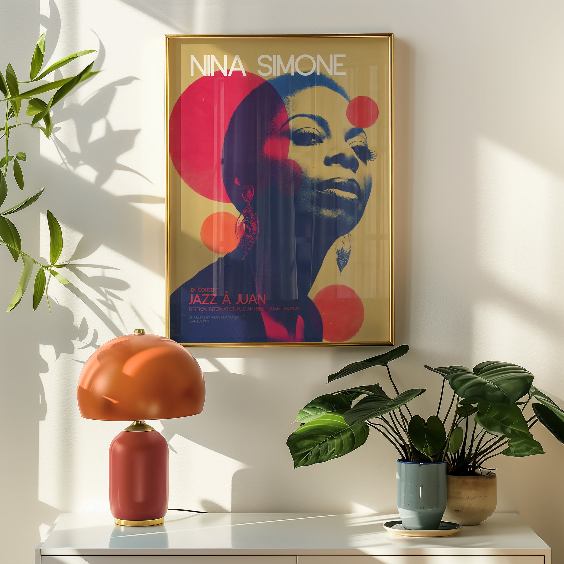 Framed Nina Simone poster on a wall with a lamp and plants below.