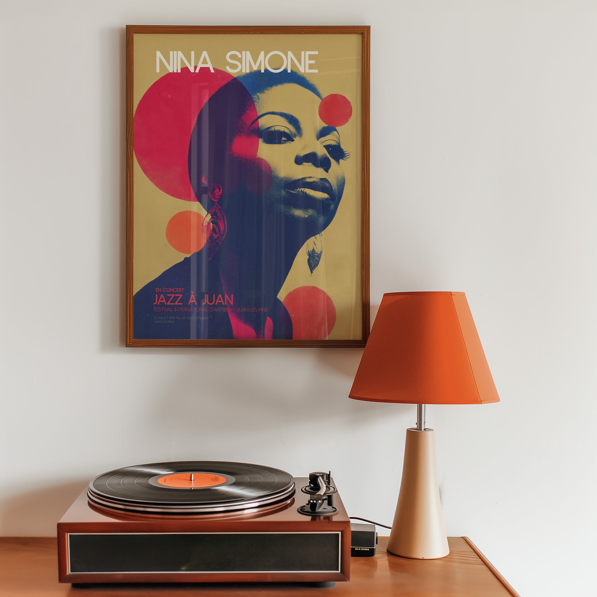 Framed Nina Simone poster above a record player with an orange lamp on a wooden surface.