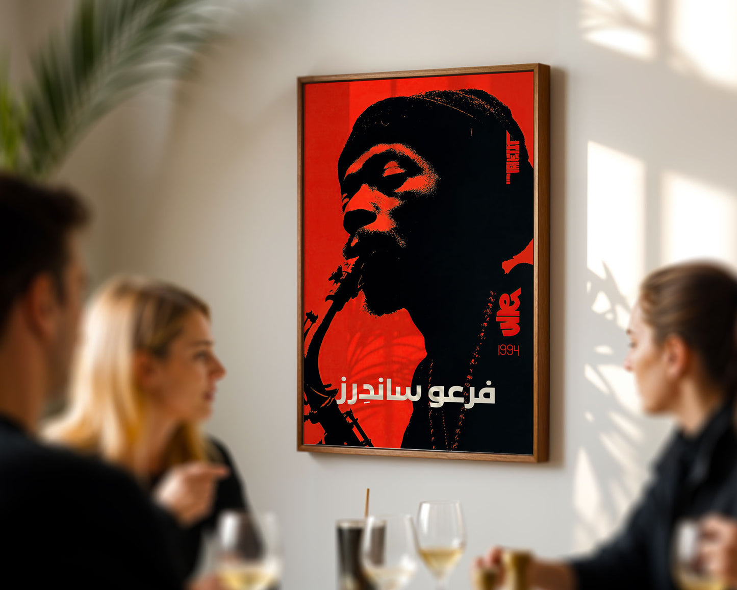 Framed poster of a stylized portrait with Arabic text in a room with people socializing.