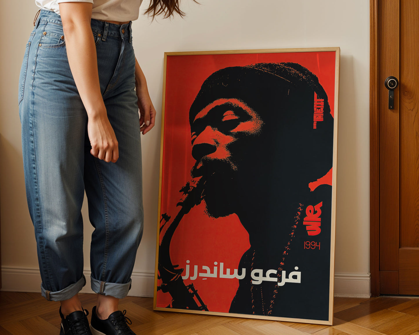 Person standing next to a framed poster of a silhouette with Arabic text on a red background.