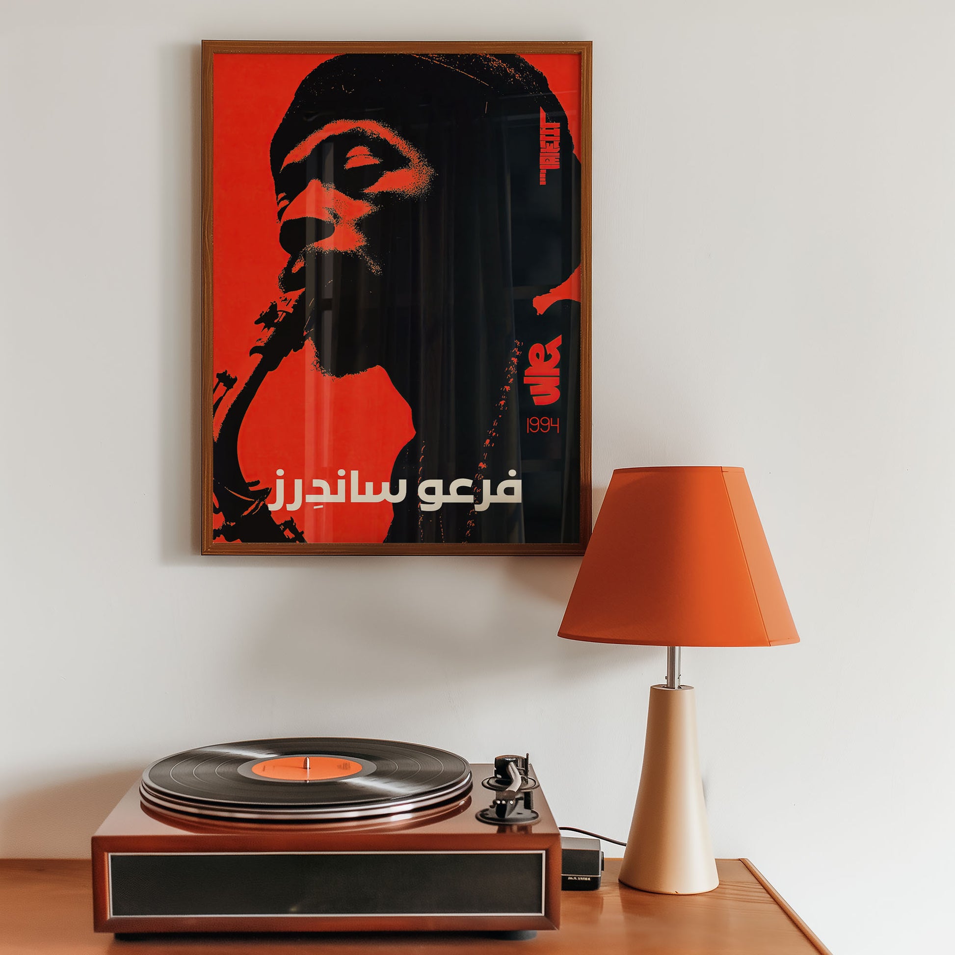 Framed artwork on a wall above a turntable with an orange lamp.