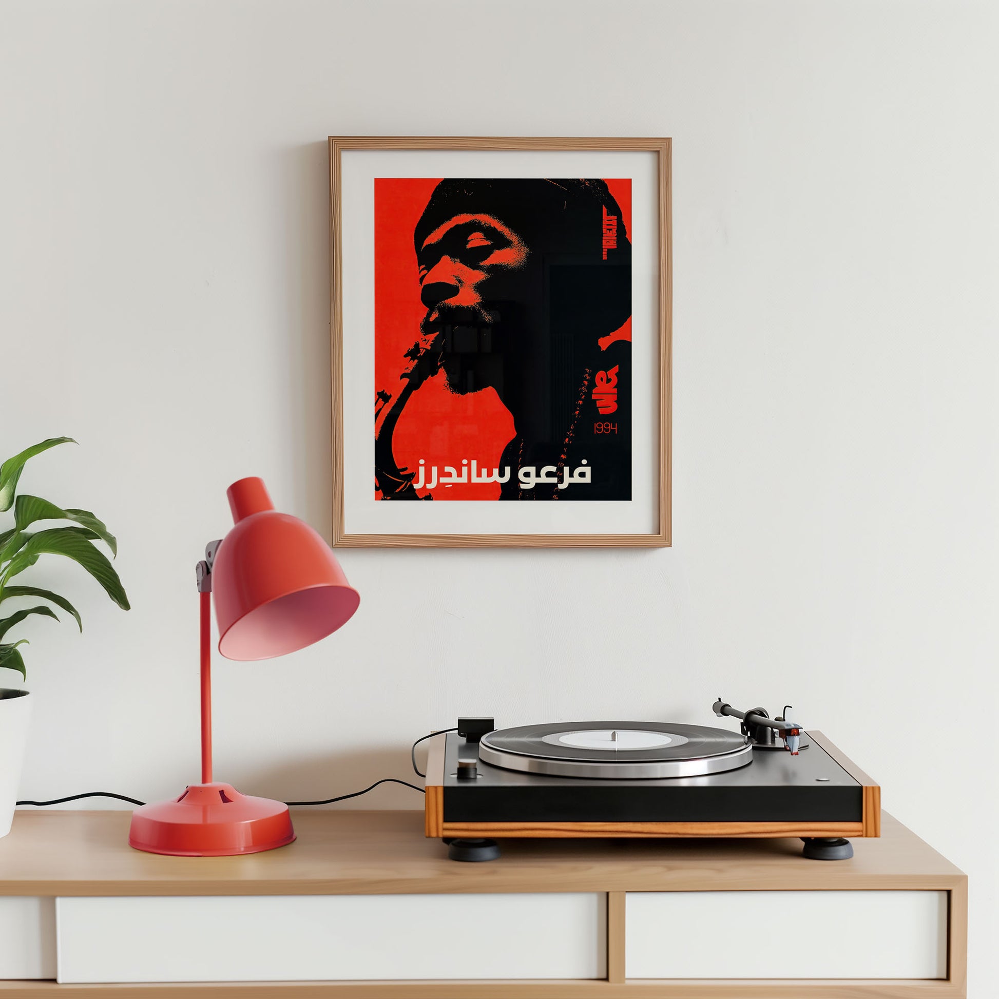 Turntable on a wooden shelf with a framed poster above it, featuring a red and black design.