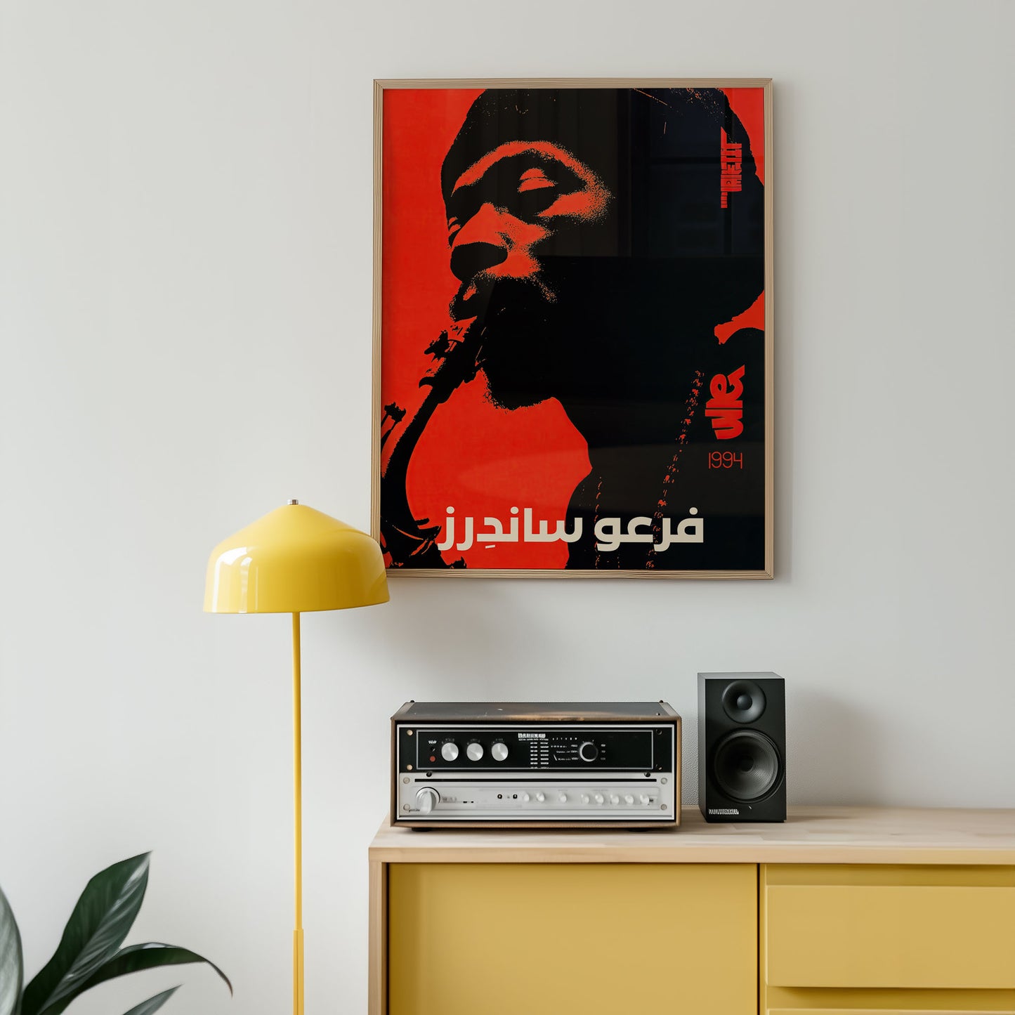 Framed artwork of a stylized face with Arabic text on a wall above a yellow cabinet with audio equipment.