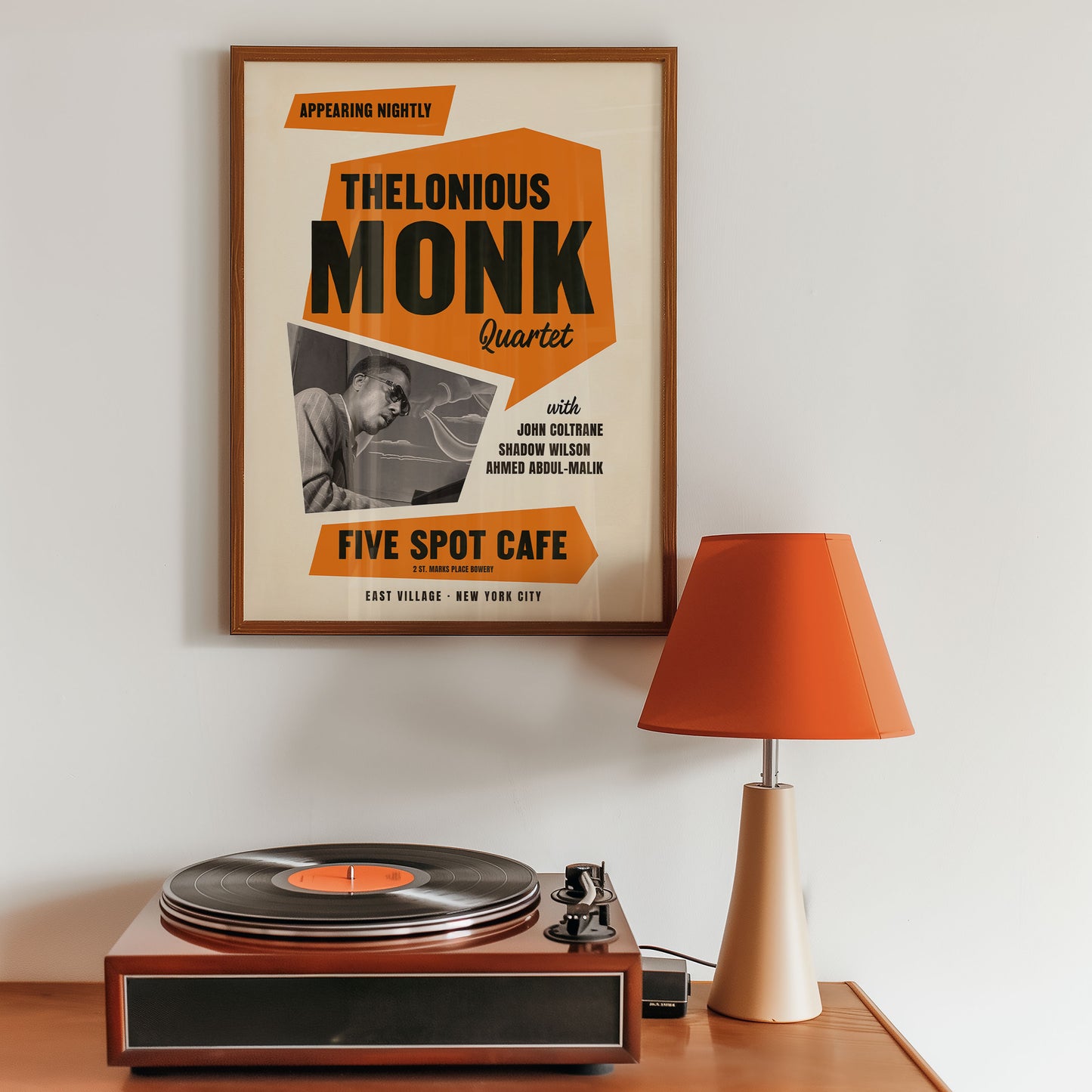  Thelonious Monk poster above a turntable with an orange lamp on a wooden surface in a music room interior. 