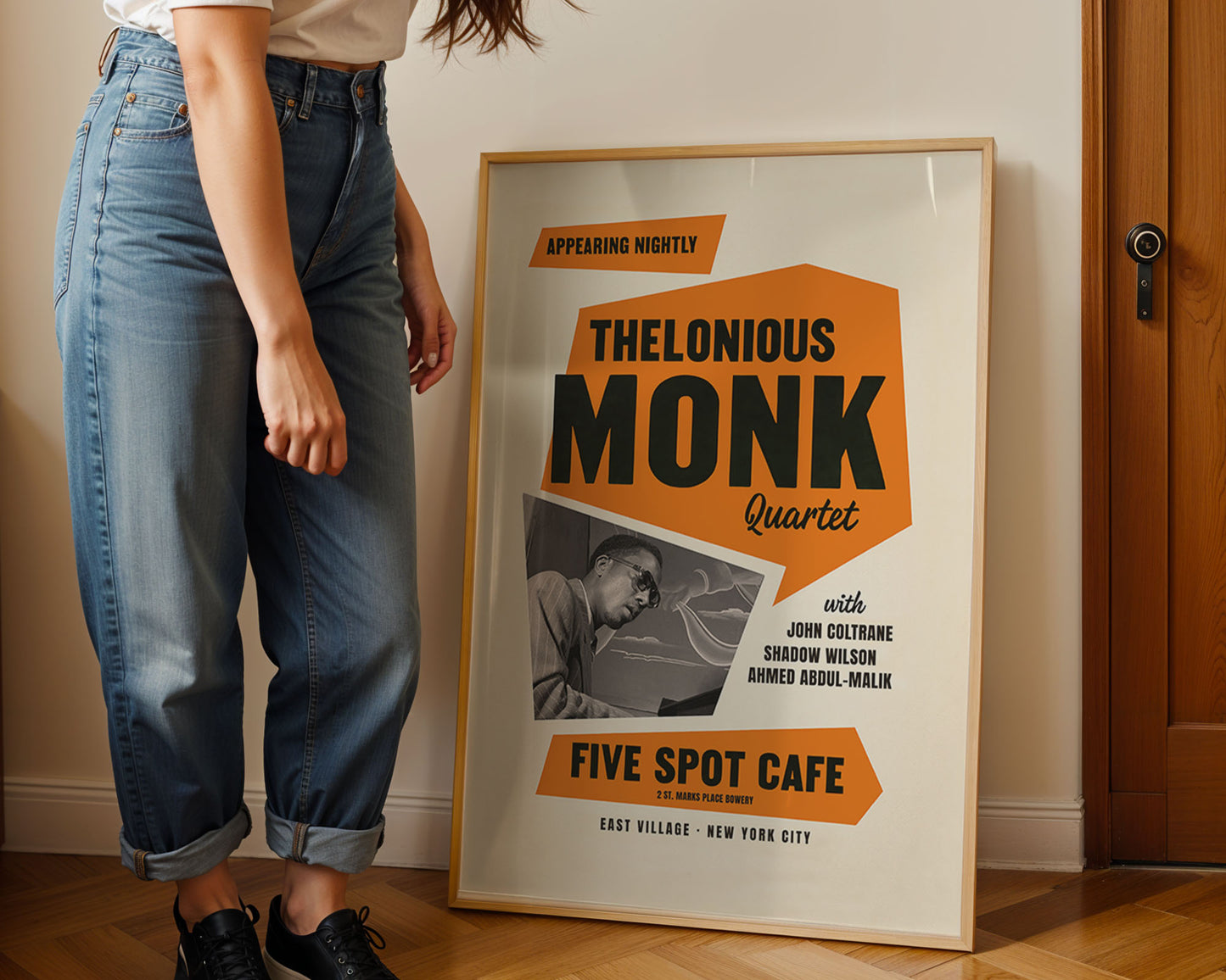 Person standing next to a framed Thelonious Monk Quartet poster on a wooden floor.