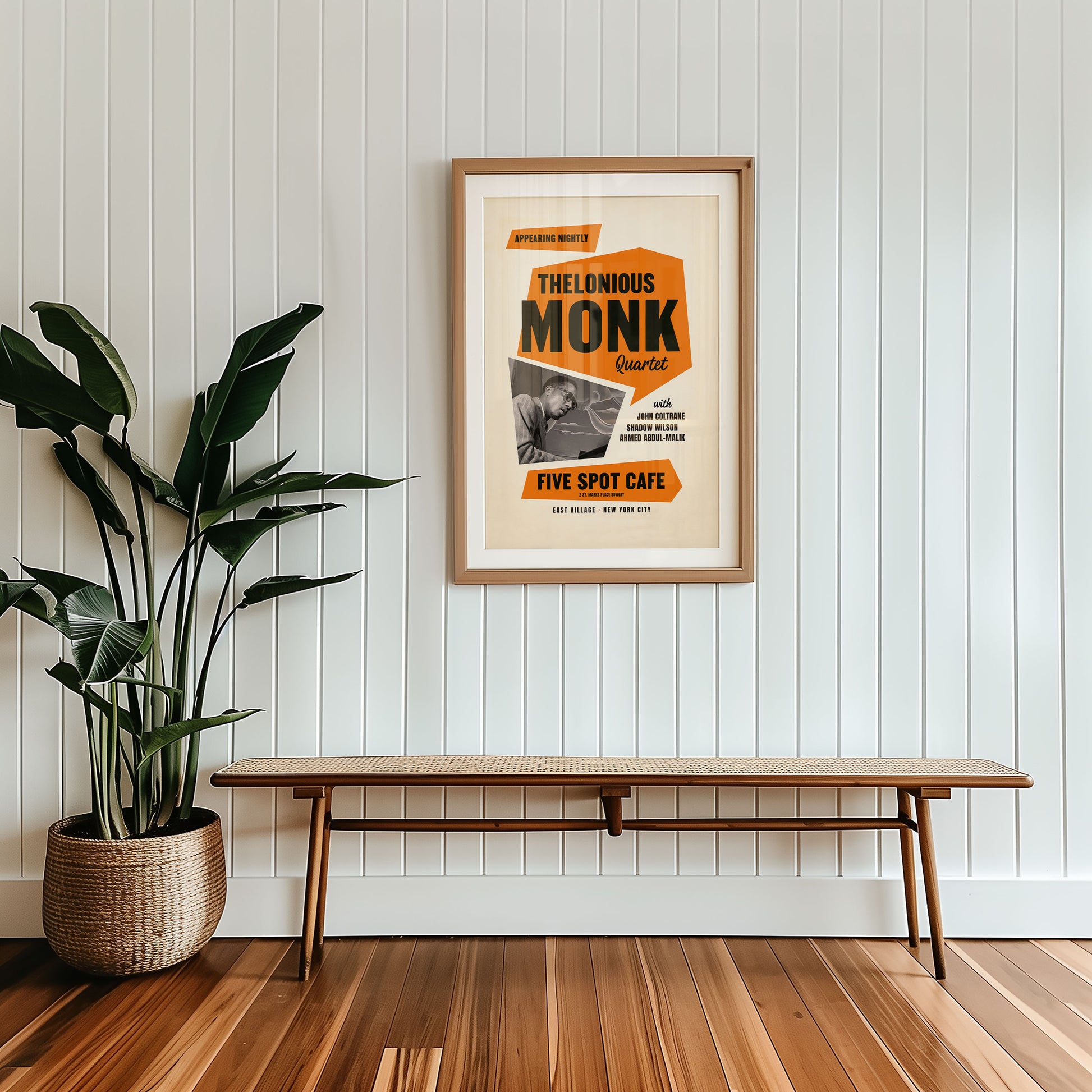 Framed poster of Thelonious Monk on a wall with a wooden bench and plant below.