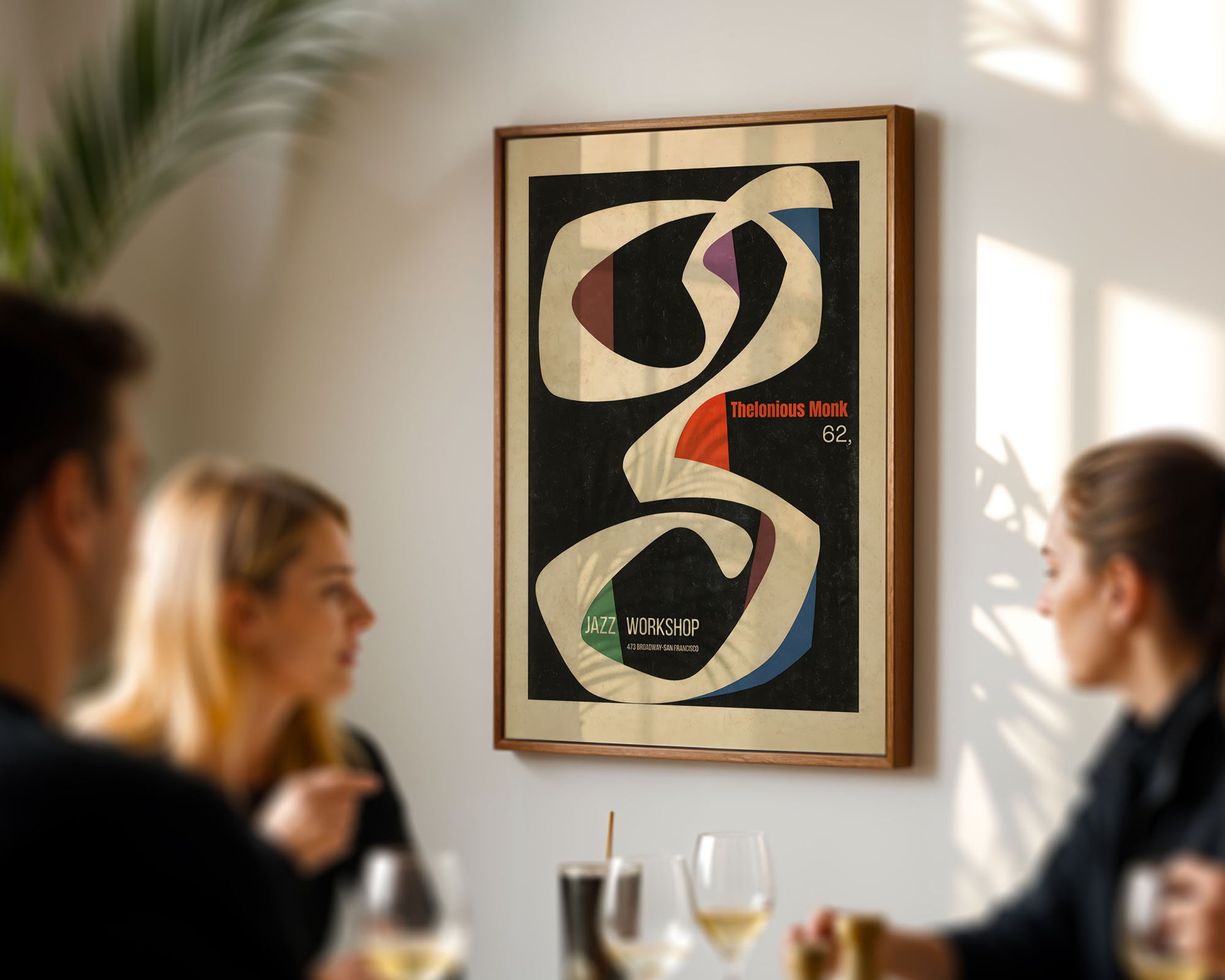 Framed abstract artwork on a wall with people socializing below