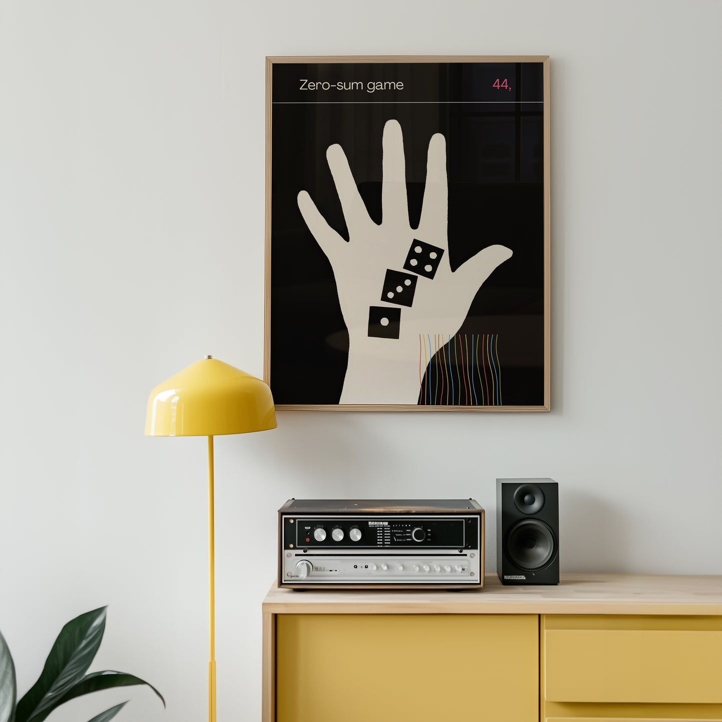 minimalist Framed artwork of a hand with dice on a wall above a yellow cabinet with audio equipment.